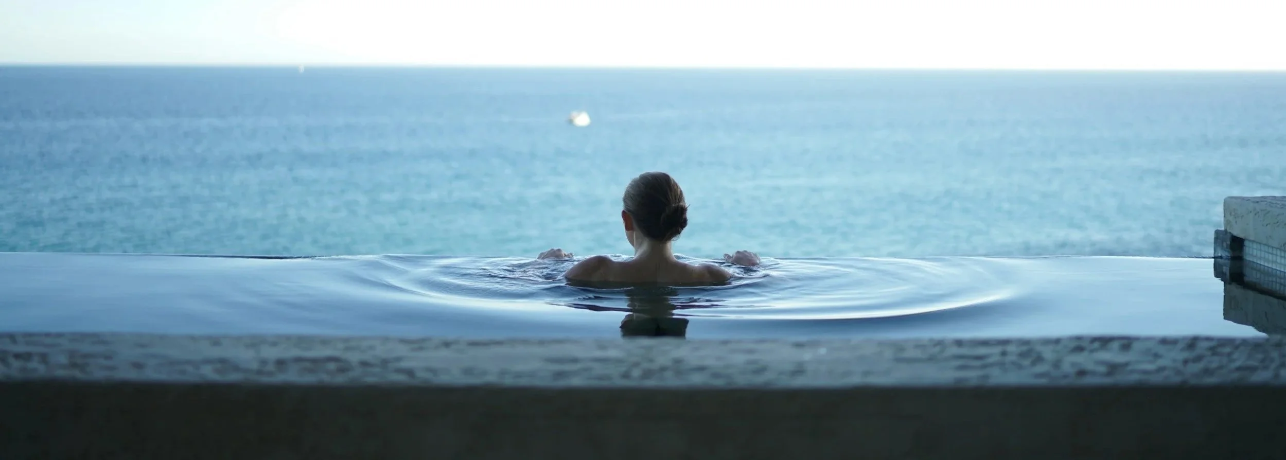 A woman in a swimming pool overlooking the ocean.