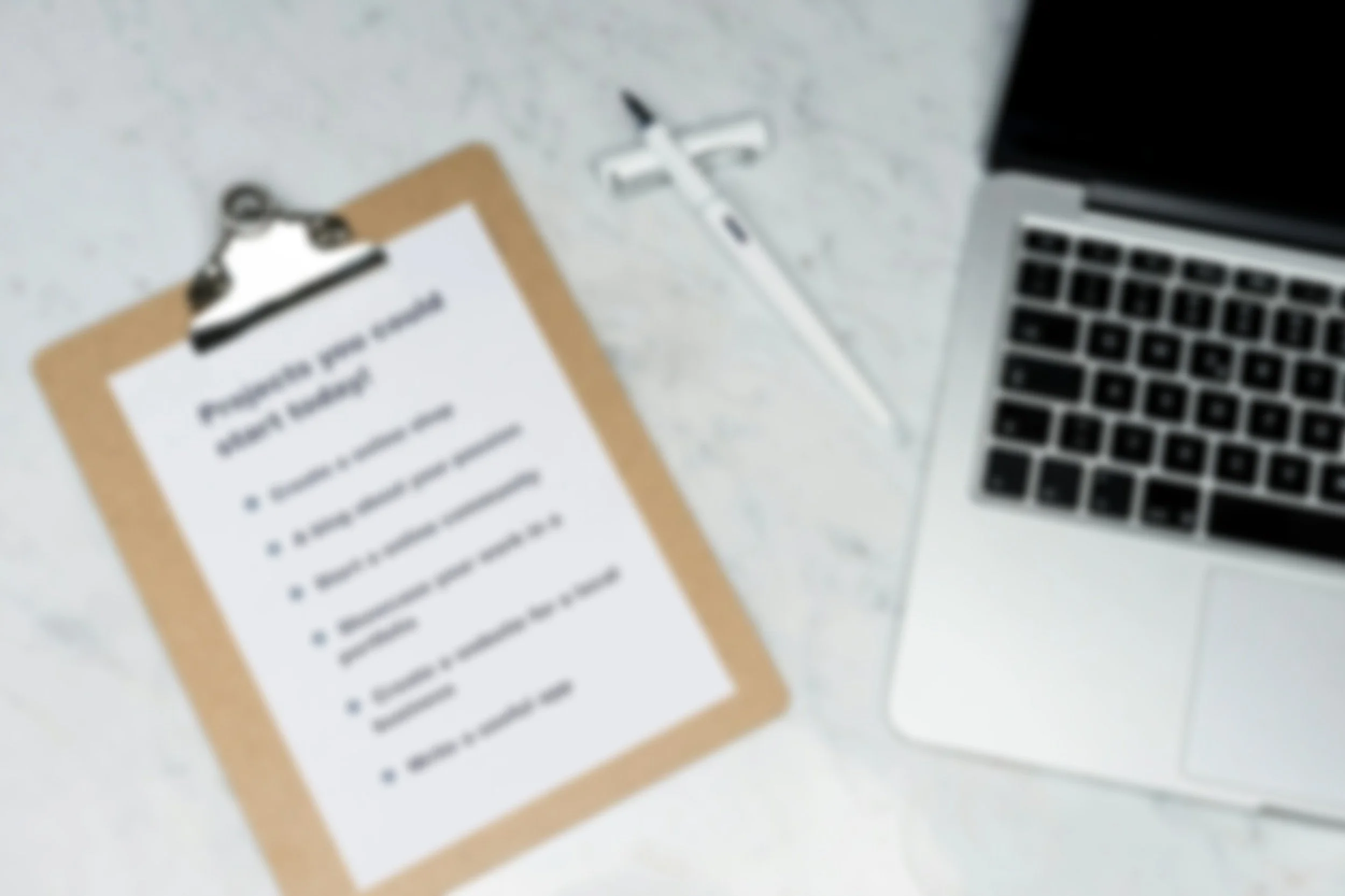 A clipboard with a printed document on it, a white disposable cup, a white pen, and a silver MacBook laptop on a white surface.