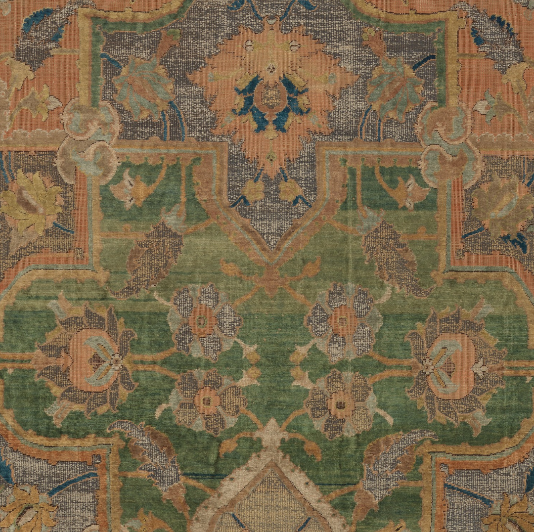 Close-up of a traditional floral patterned rug with green, tan, orange, beige, blue, and dark brown colors.