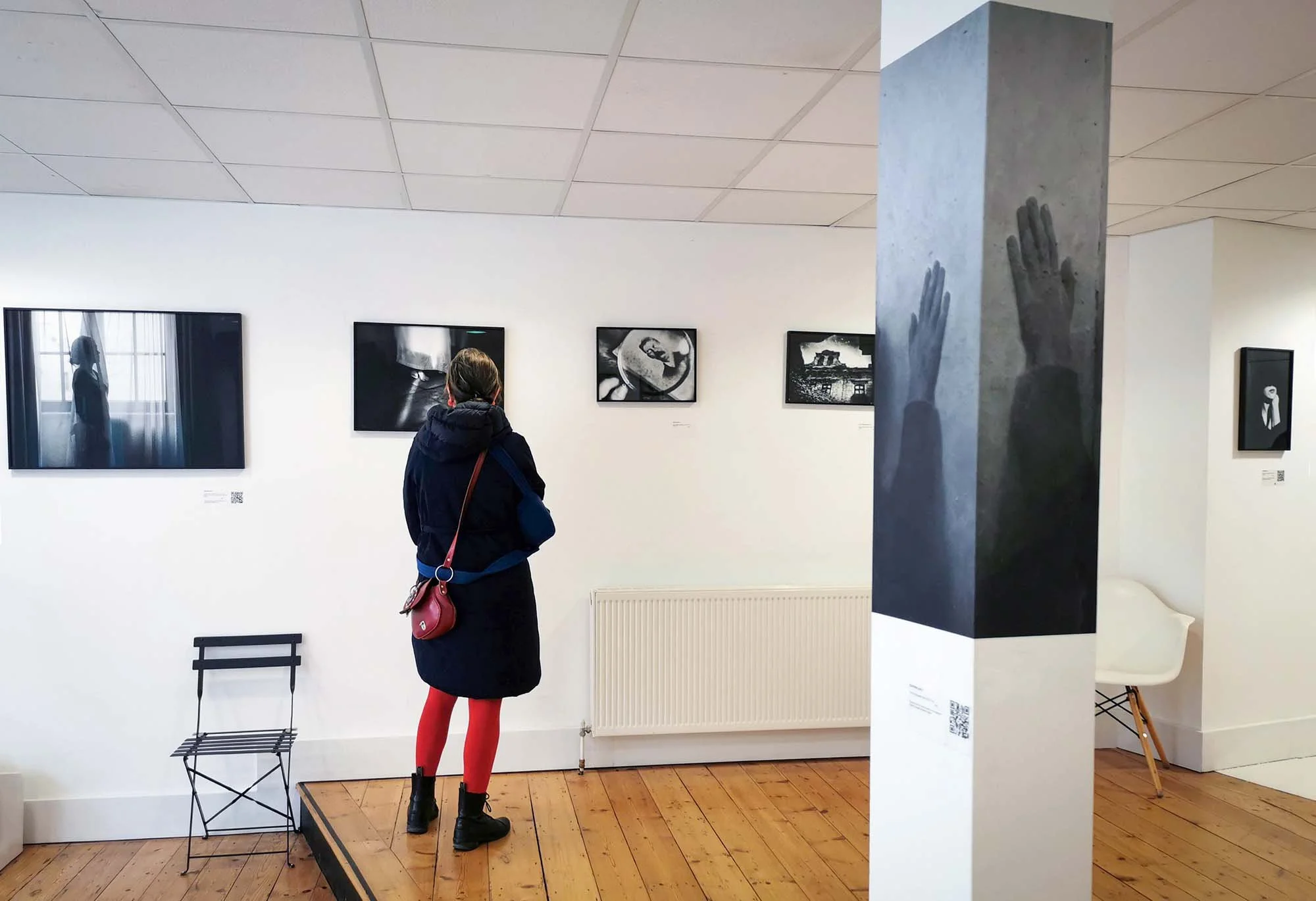 Installation view of I Also Fight Windmills, with black-and-white photographs displayed throughout a gallery and a visitor viewing the work.
