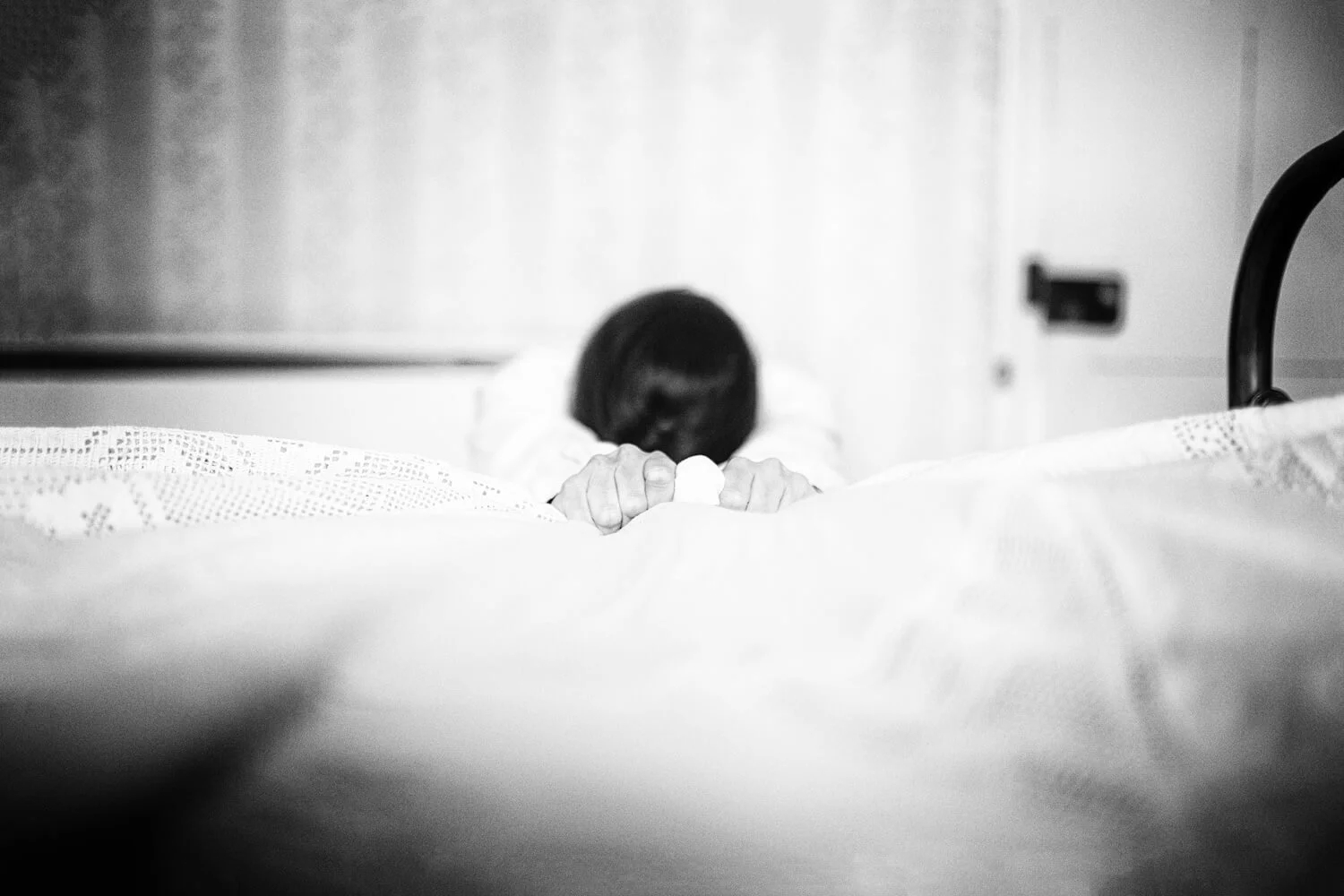 Detail of Slipping by Ania Ready, showing a woman gripping the edge of a bed with only her head and hands visible.