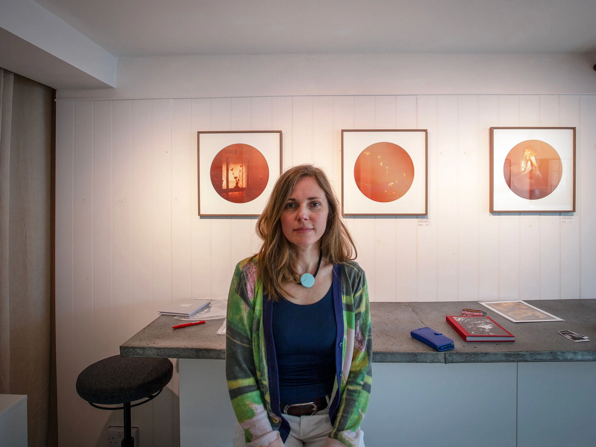 Artist Ania Ready photographed in a gallery with her work displayed behind her.