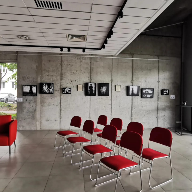 Gallery talk setting with rows of red chairs facing an exhibition of photographic works.