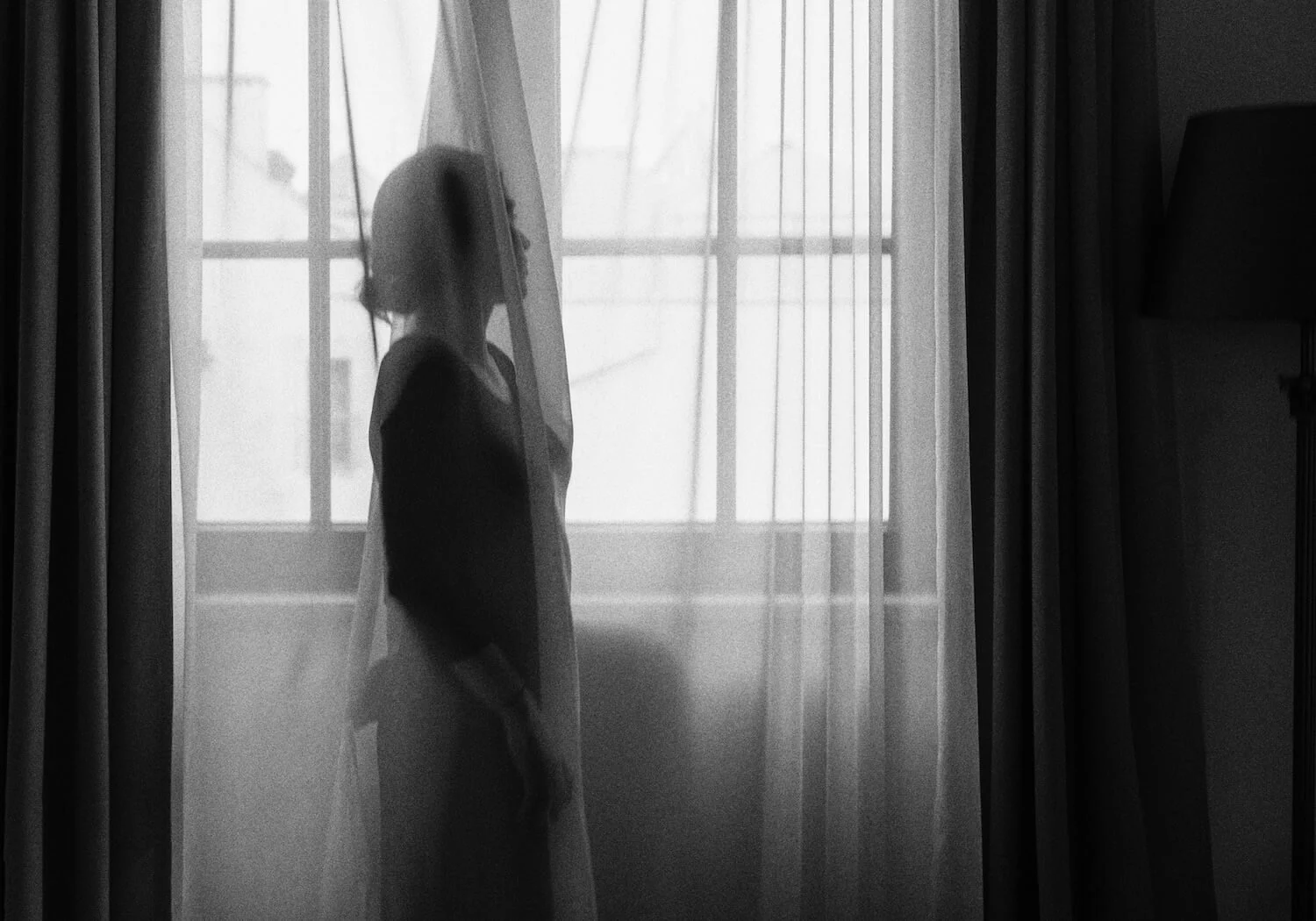 Detail of Veiled by Ania Ready, showing the woman’s silhouette framed by a window and translucent curtain.