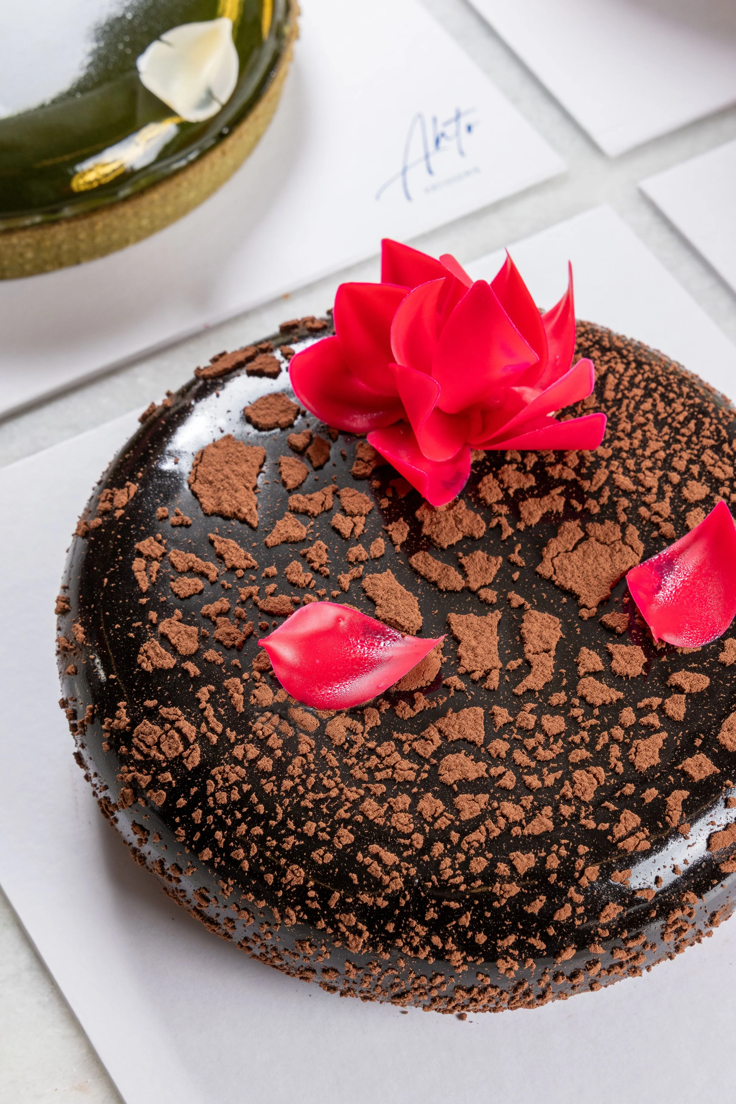 Entremet de chocolate da Ahto Pâtisserie, decorado com flor de chocolate e pétalas, representando a seleção de entremets da pâtisserie em São Paulo.