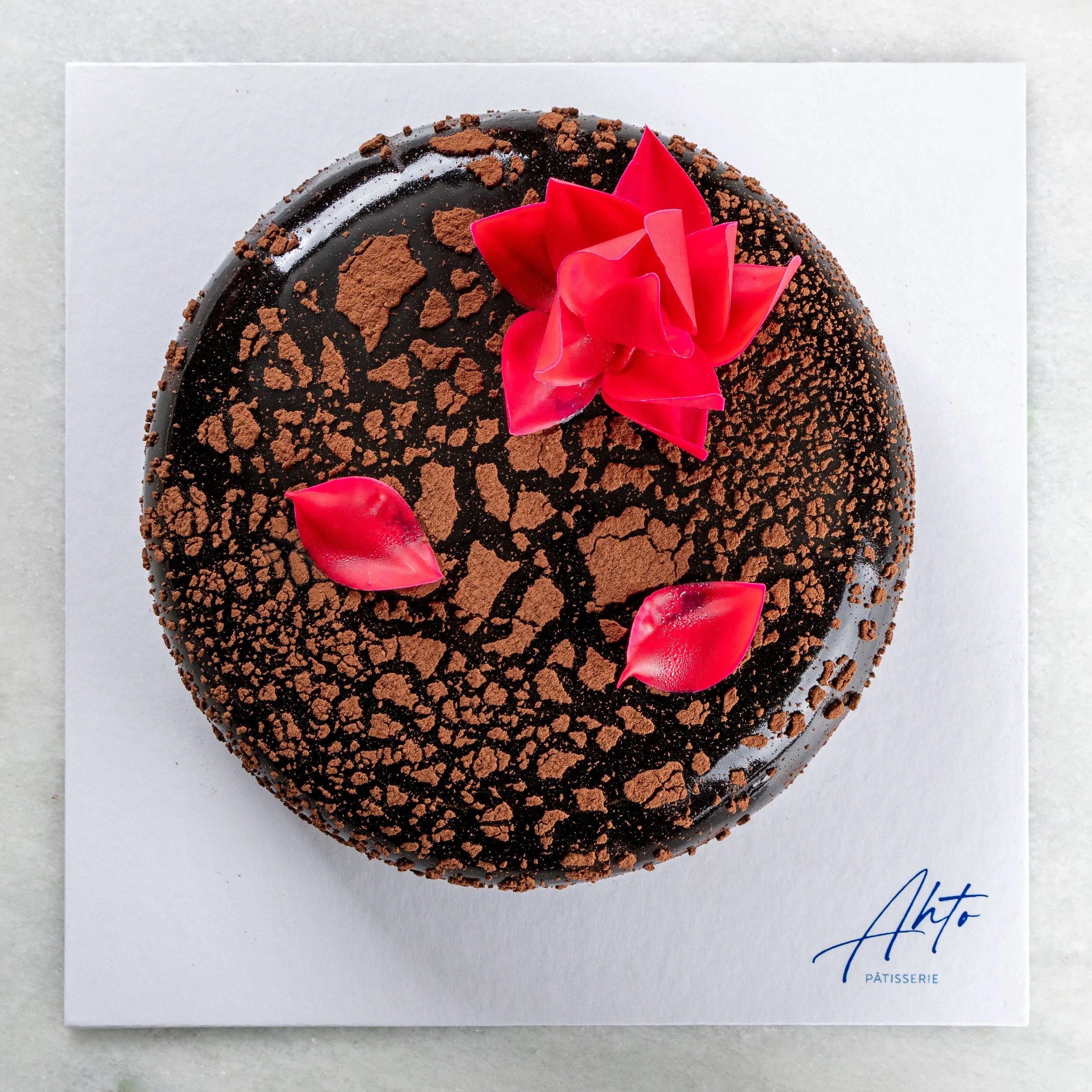 Entremet Noir da Ahto Pâtisserie, releitura da Floresta Negra com acabamento de chocolate e decoração floral vermelha.