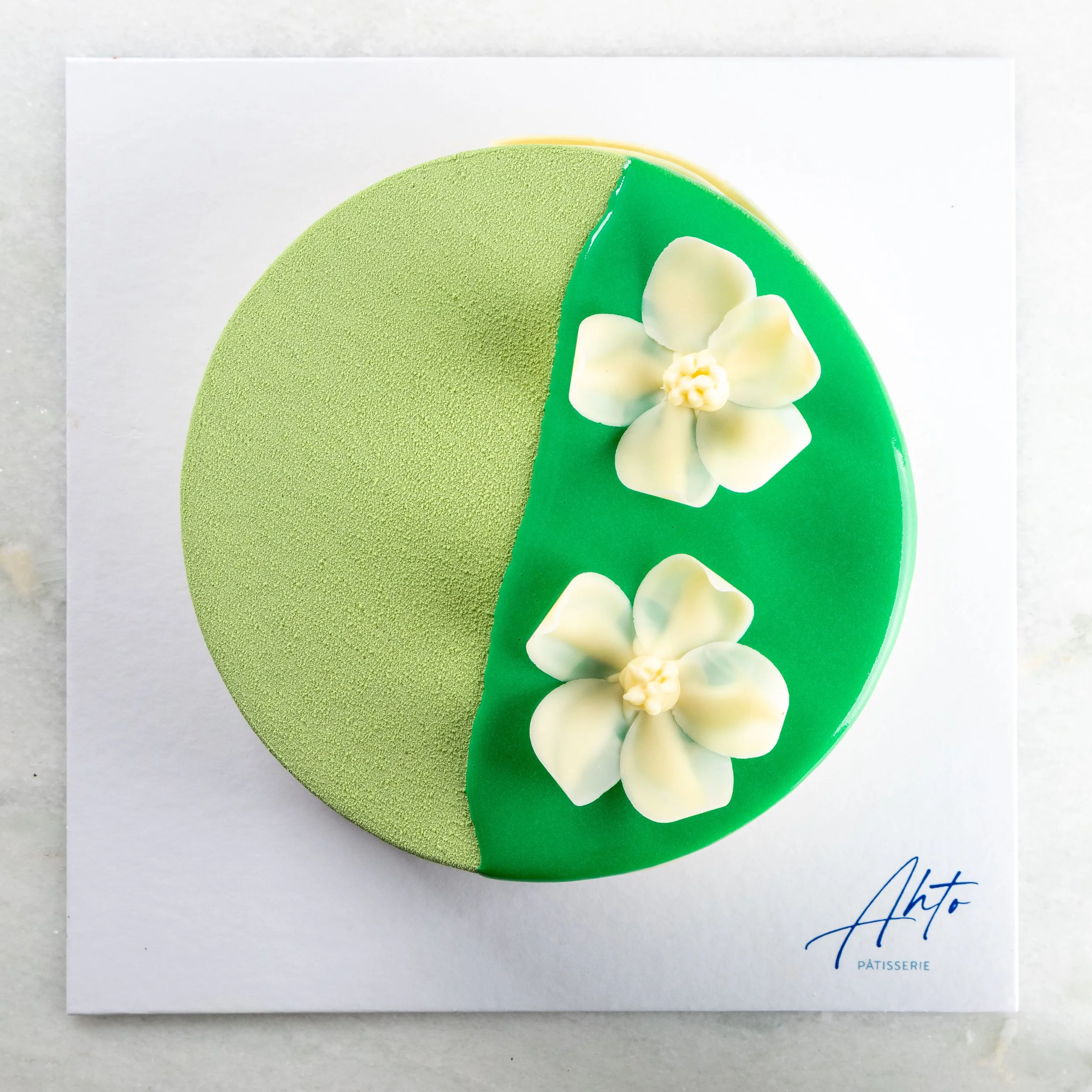 Entremet Trio da Ahto Pâtisserie, com acabamento verde de matcha e flores brancas de chocolate.