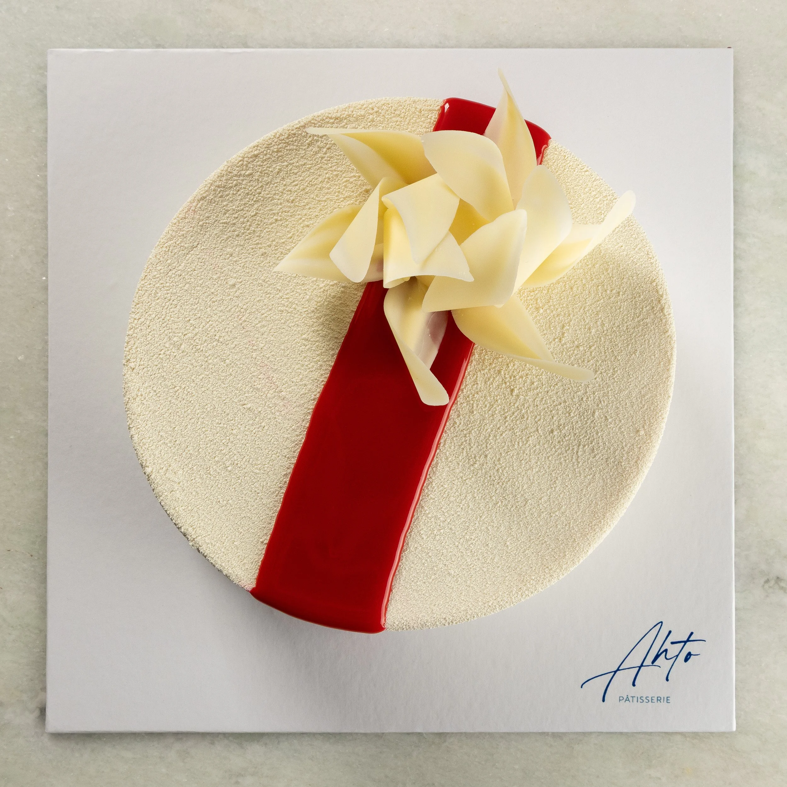 Entremet Framboise da Ahto Pâtisserie, com acabamento branco, detalhe vermelho e decoração de chocolate.