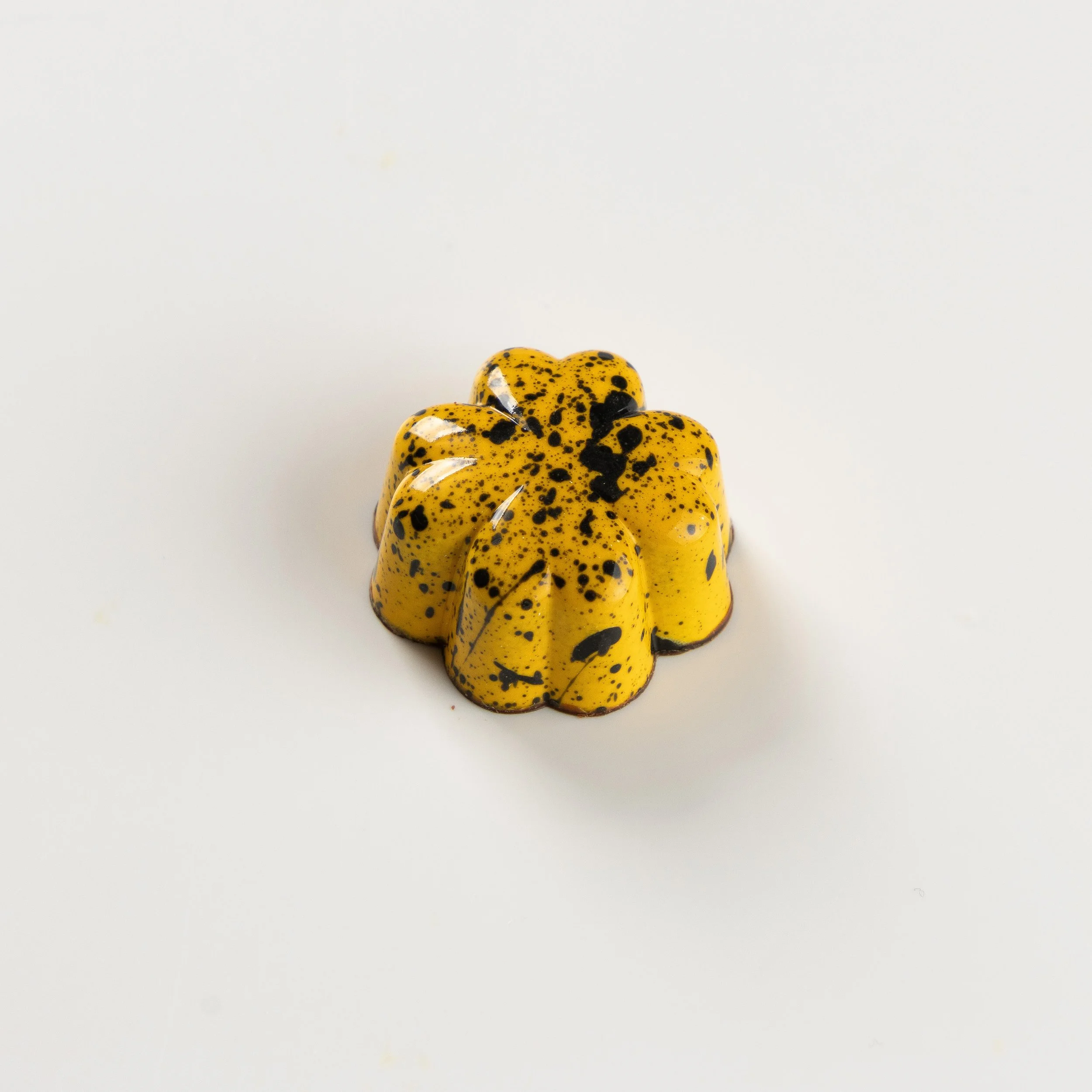 Bombom de maracujá da Ahto Pâtisserie, com acabamento amarelo e detalhes escuros.