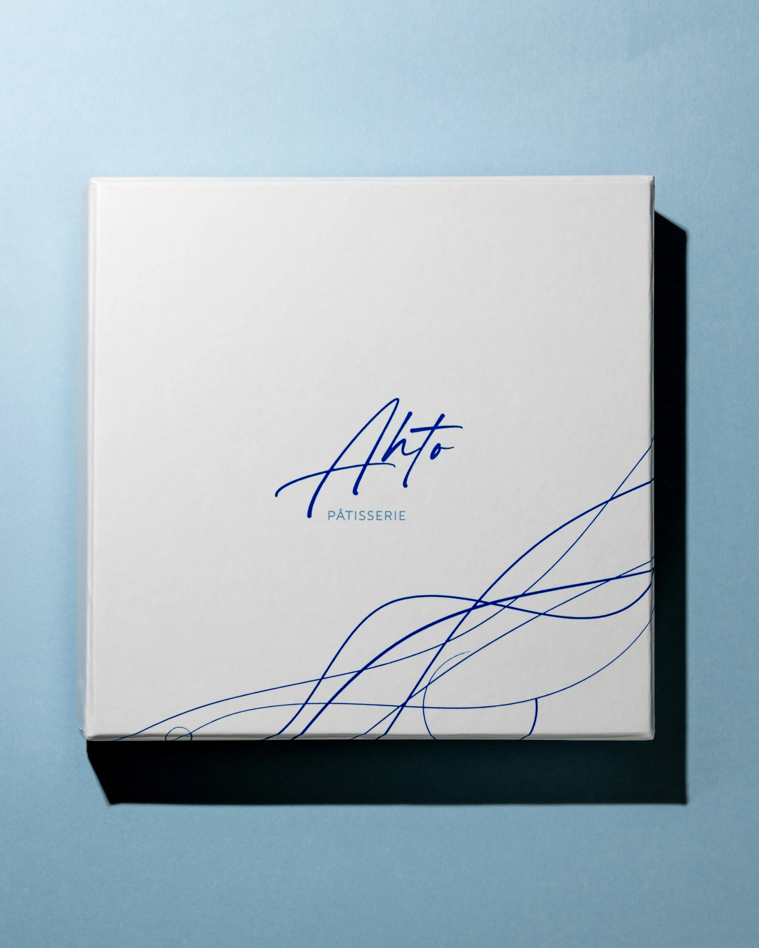 Caixa para presente da Ahto Pâtisserie, com identidade visual da marca em branco e azul.