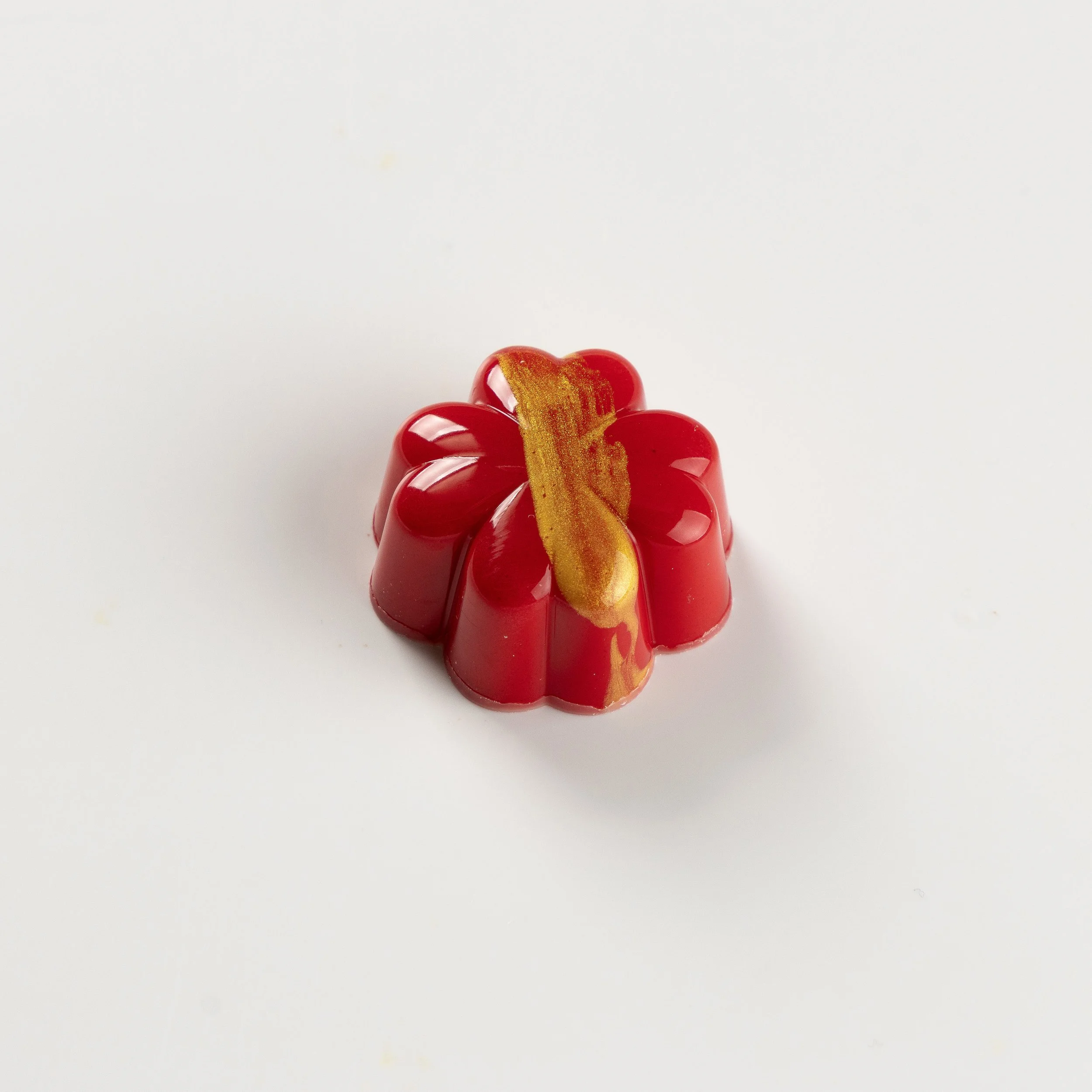 Bombom de morango da Ahto Pâtisserie, com acabamento vermelho e detalhe dourado.