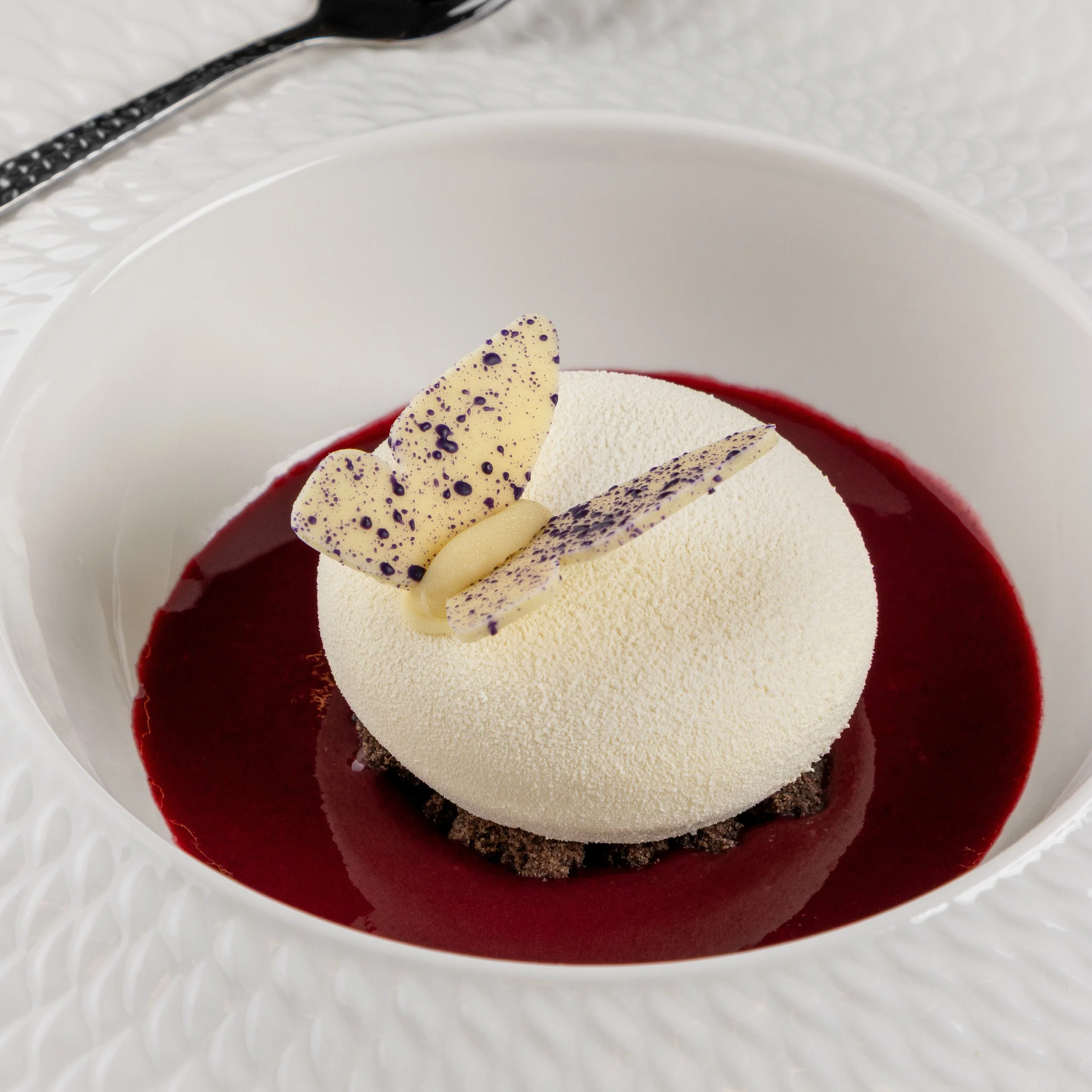 Sobremesa autoral criada pela Ahto Pâtisserie para restaurante, com mousse, decoração de chocolate e apresentação em molho de frutas vermelhas.