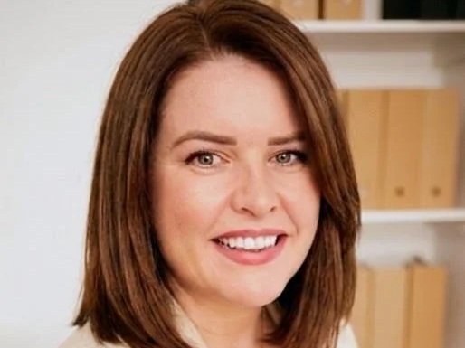 A woman with shoulder-length brown hair smiling in front of a bookshelf.