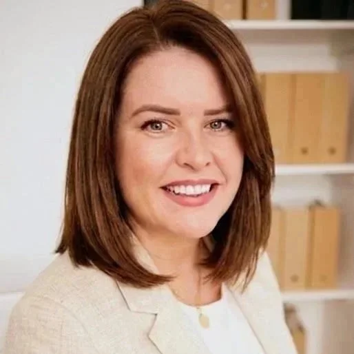Headshot of a woman with shoulder-length brown hair, smiling, in front of a bookshelf with binders.