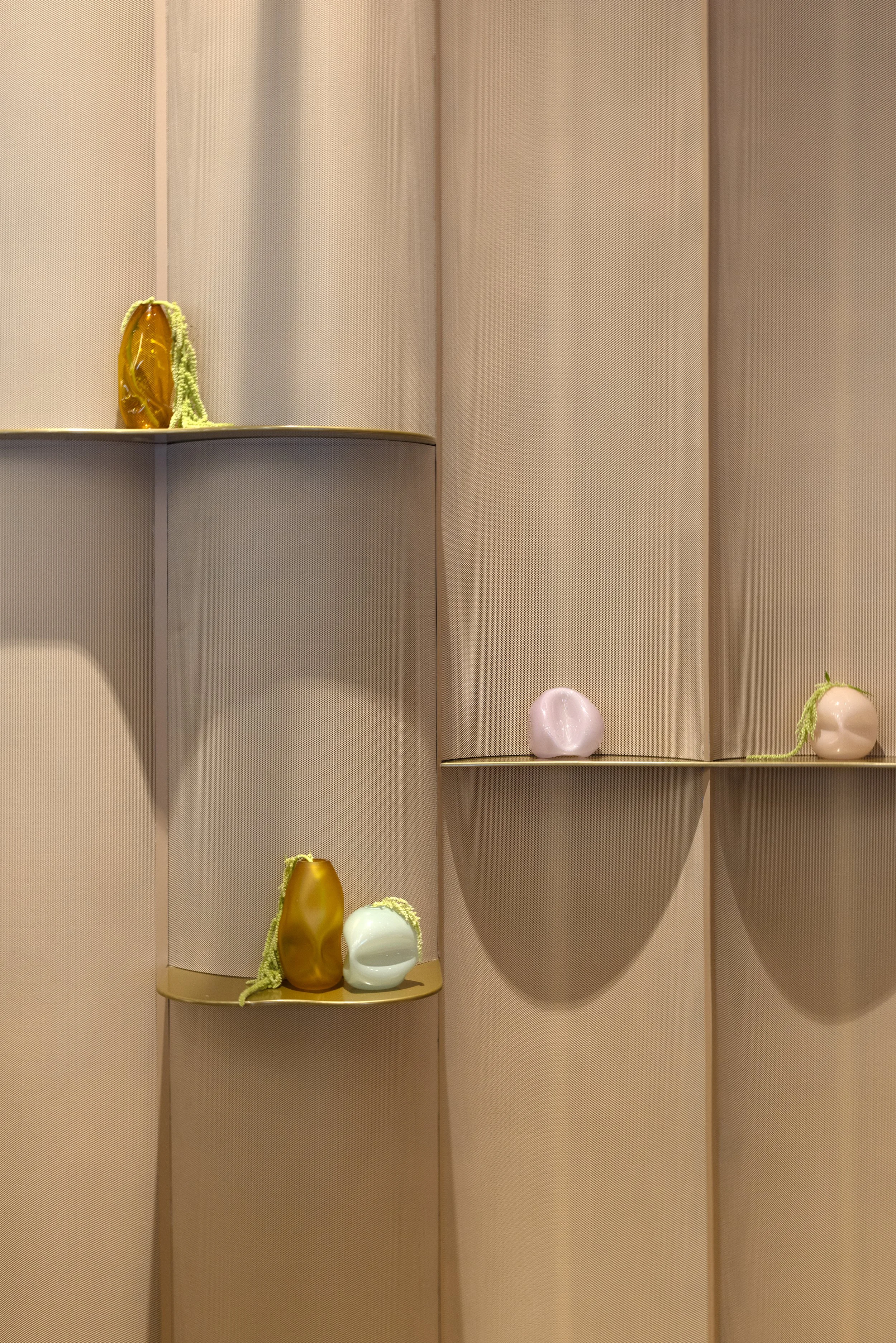 A display shelf with decorative vases in various shapes and colors, some with green plant-like decorations, against a beige textured wall.