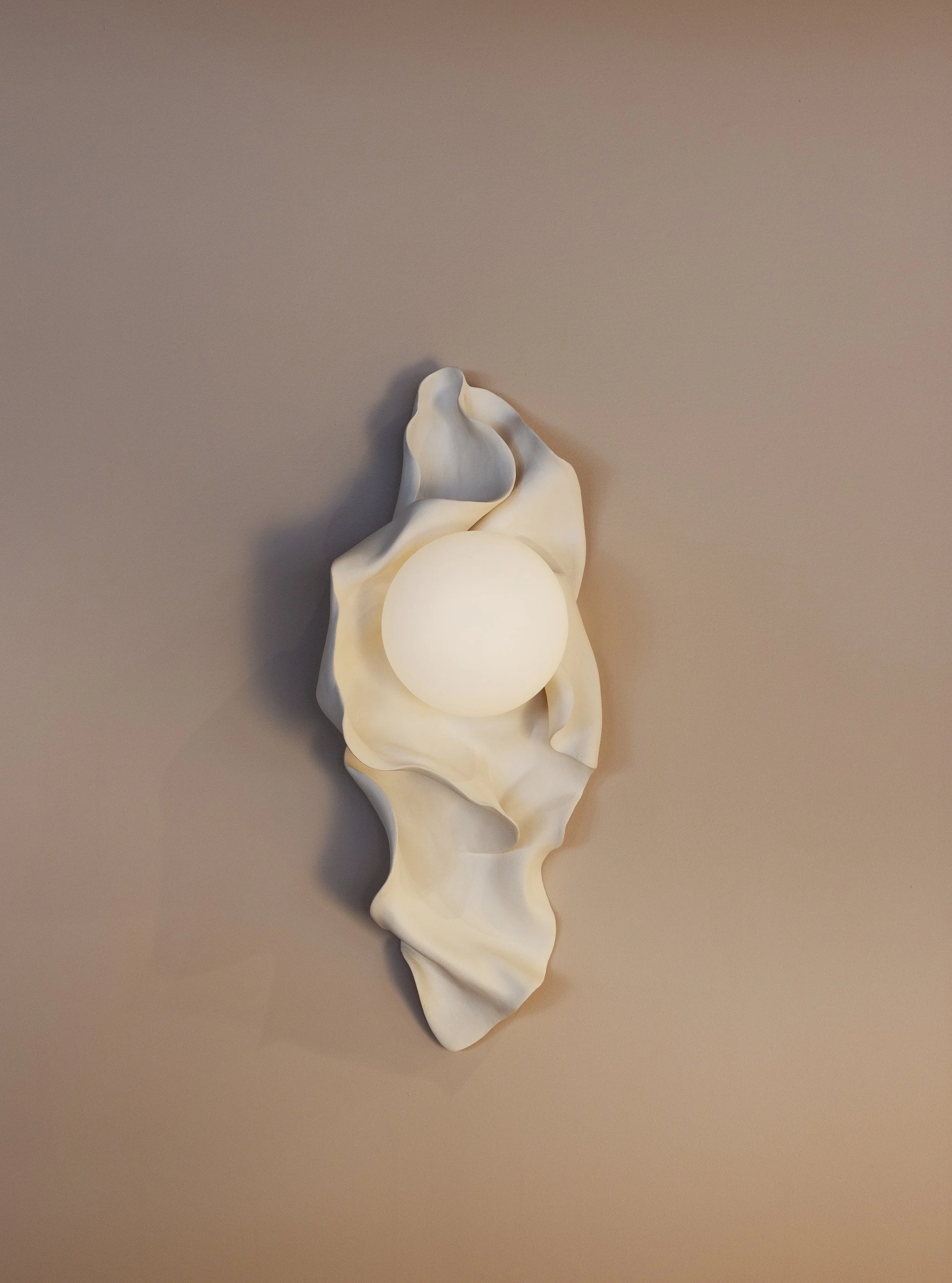 A white ceramic sculpture resembling a flower with a spherical light bulb at its center, set against a plain, neutral background.