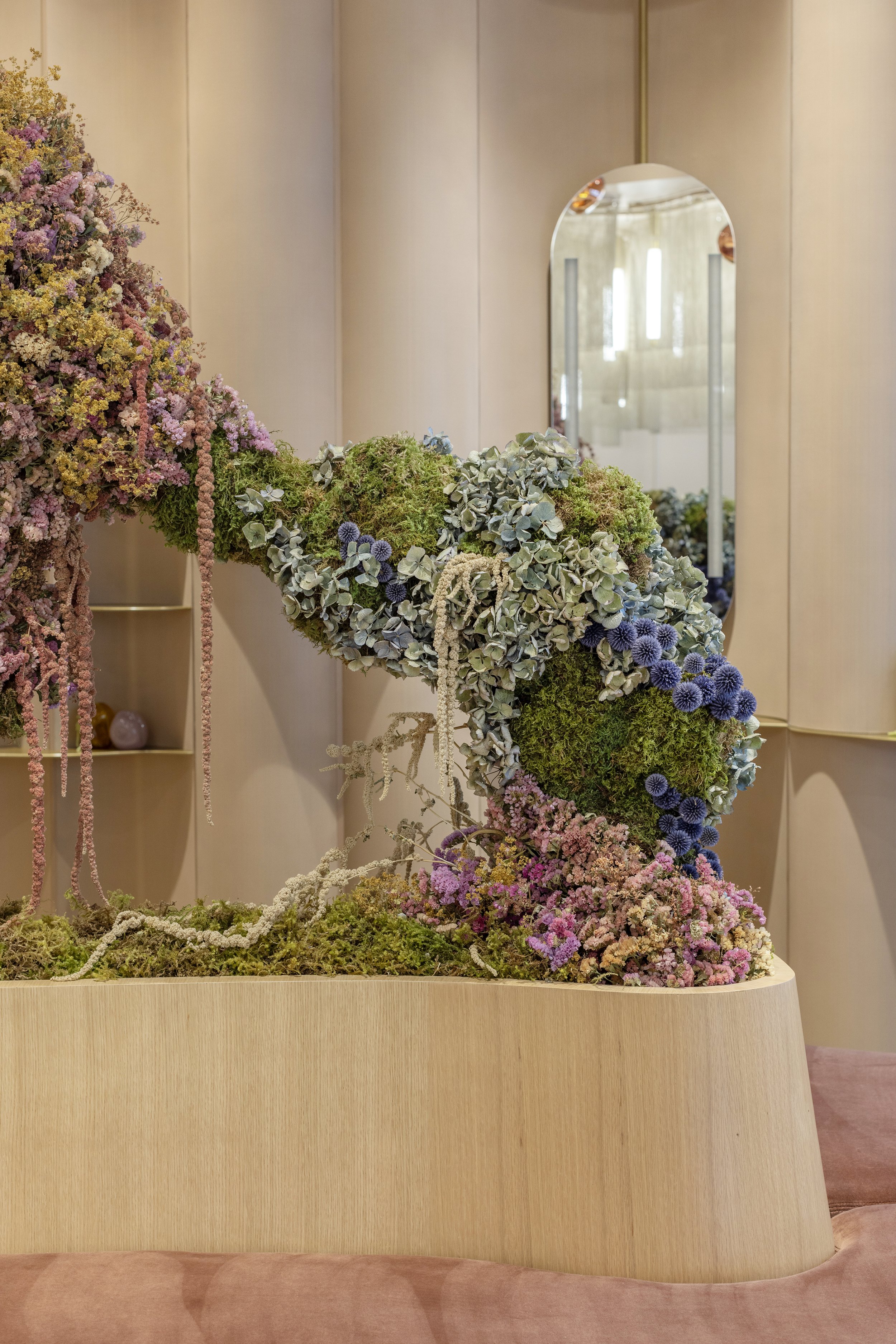 Decorative floral arrangement on a wooden stand with a mirror in the background.