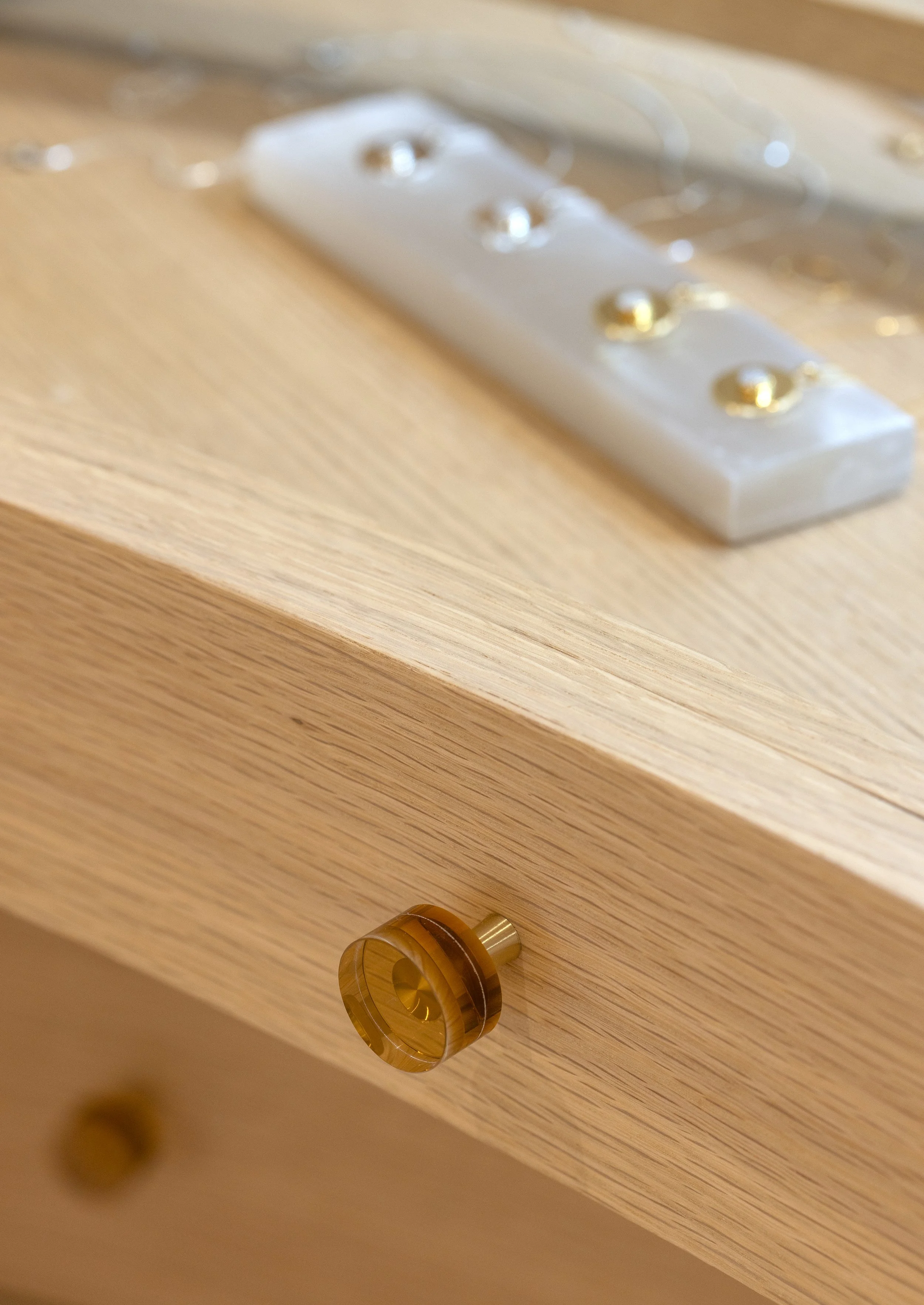 Close-up of a wooden drawer with a round, amber-colored handle and a white marble top with gold accents.