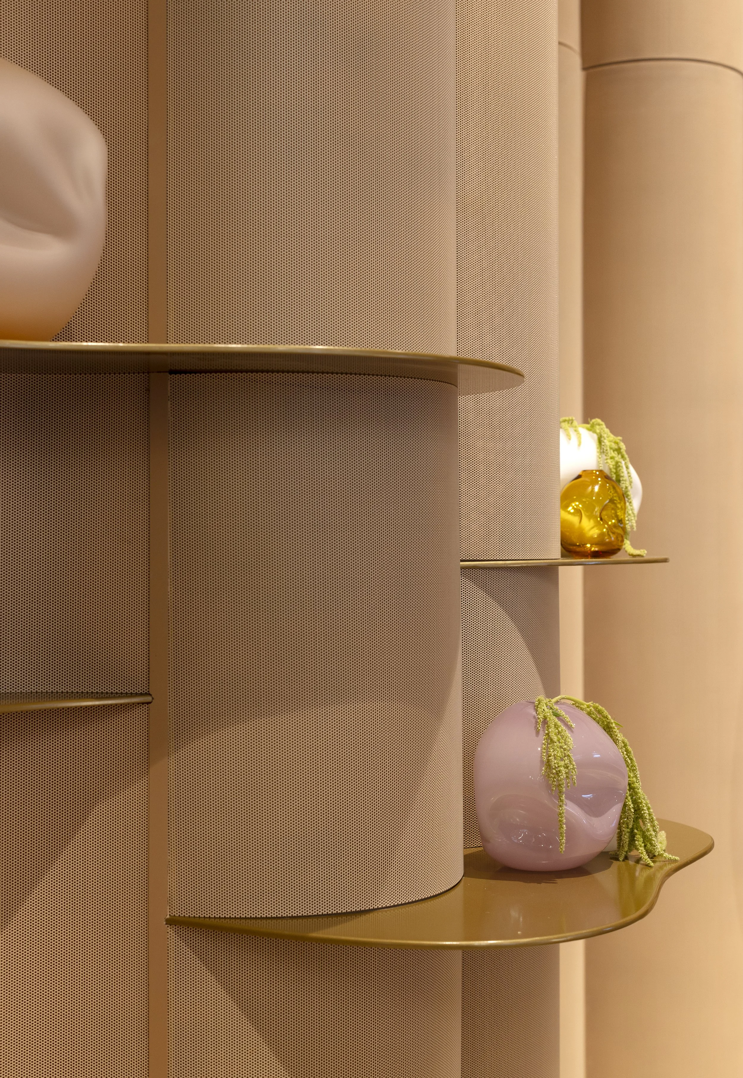 Display shelf with decorative items, including a pink heart-shaped vase with green trailing plants, set against a perforated beige wall.