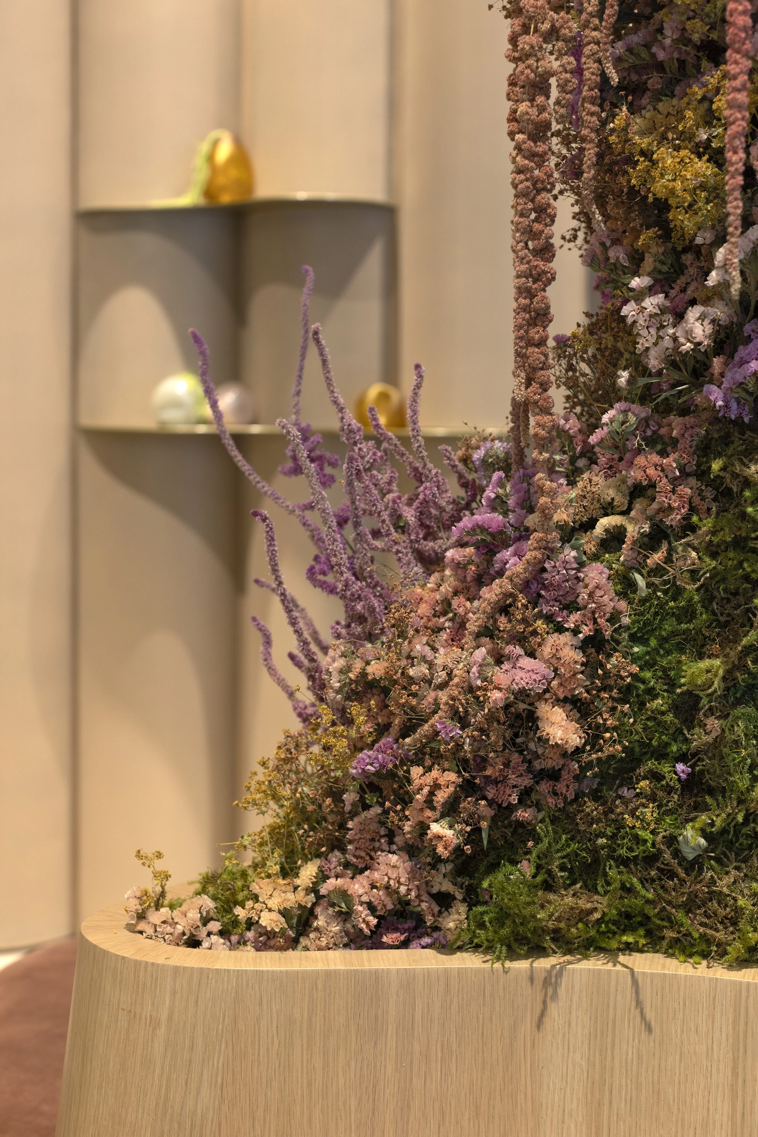 A large arrangement of pink, purple, and yellow flowers displayed in a wooden container.