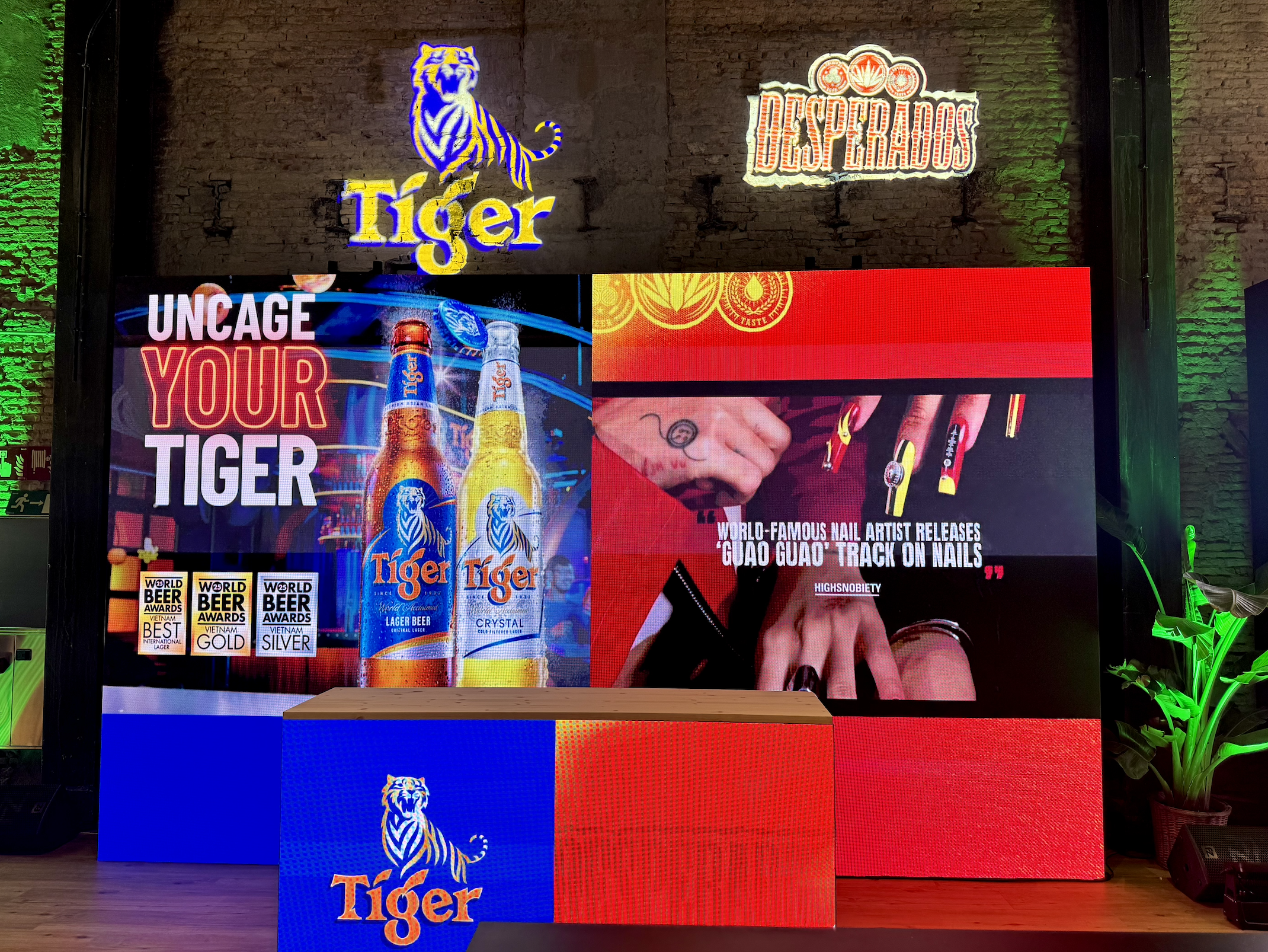 Neon signs on a brick wall, including a tiger logo with the word "Tiger," a sign for "Desperados," and a promotional display for Tiger beer bottles with the phrase "Uncage your tiger" and award medals.