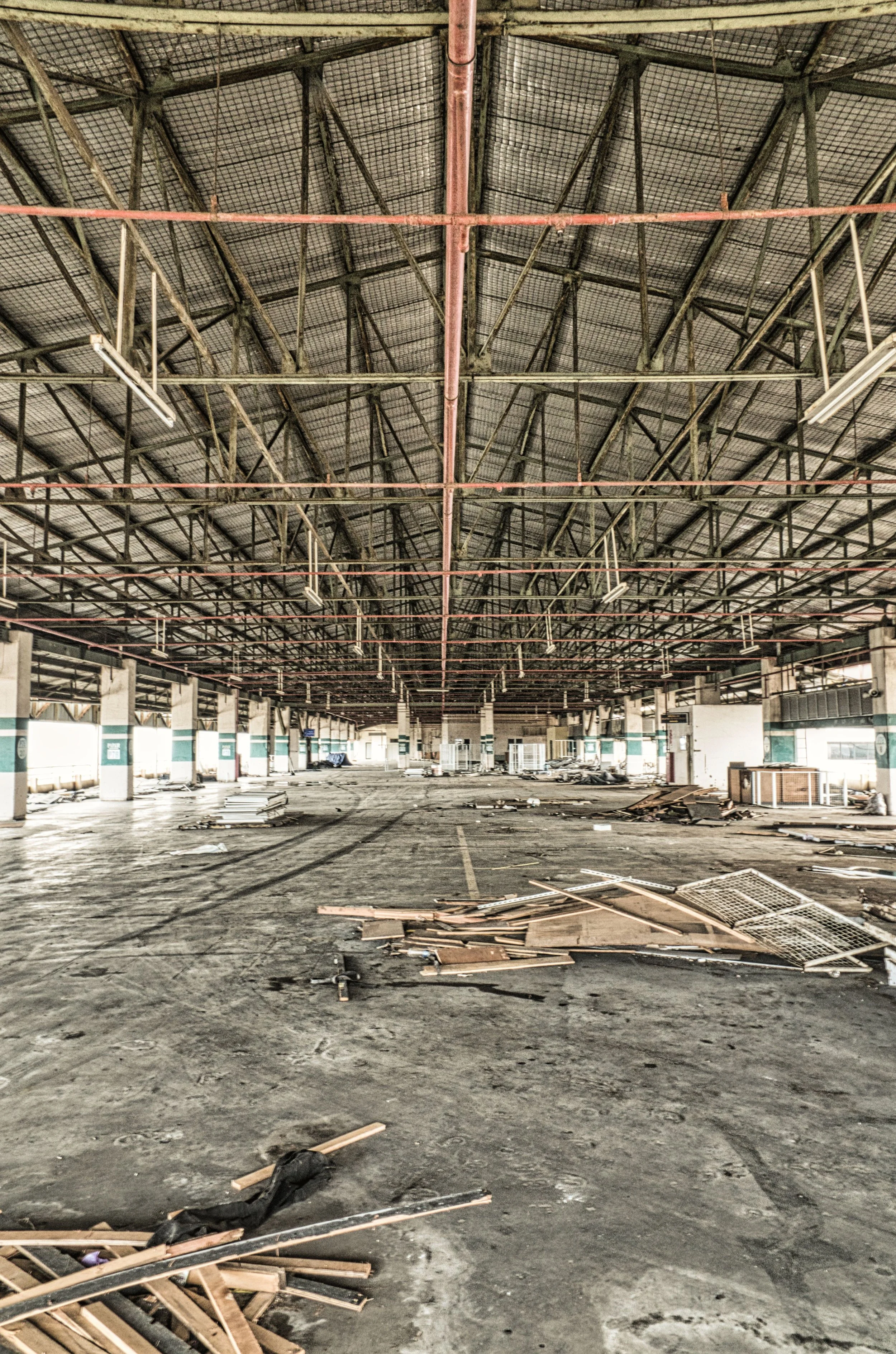 Interior of an abandoned large parking garage with debris scattered on the floor and a high ceiling with metal support beams.