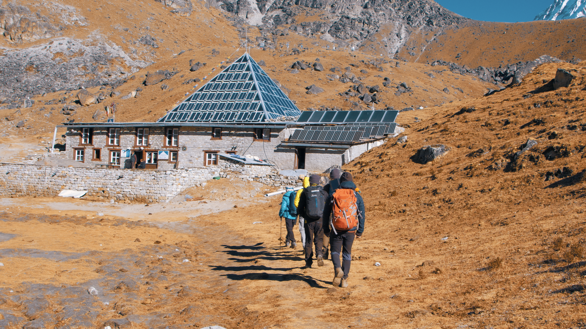 Des hommes marchent de dos vers un bâtiment pyramidal dans une plaine de haute altitude