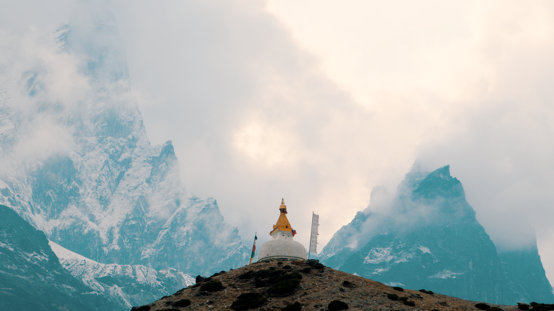 Un temple au sommet d'une colline, avec des montagnes enneigées en arrière-plan, entouré de brouillard et de nuages.