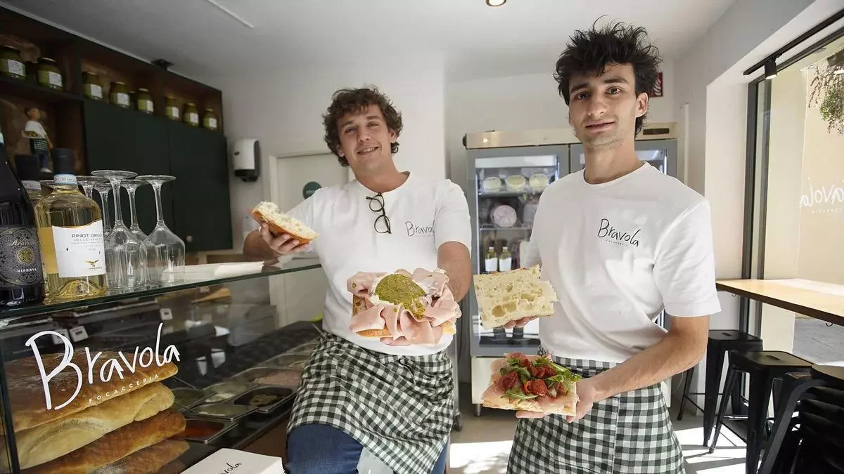 Javier y Ferran, los propietarios sosteniendo platos con las focaccias mas vendidas, delante del mostrador expositor con los ingredientes expuestos.