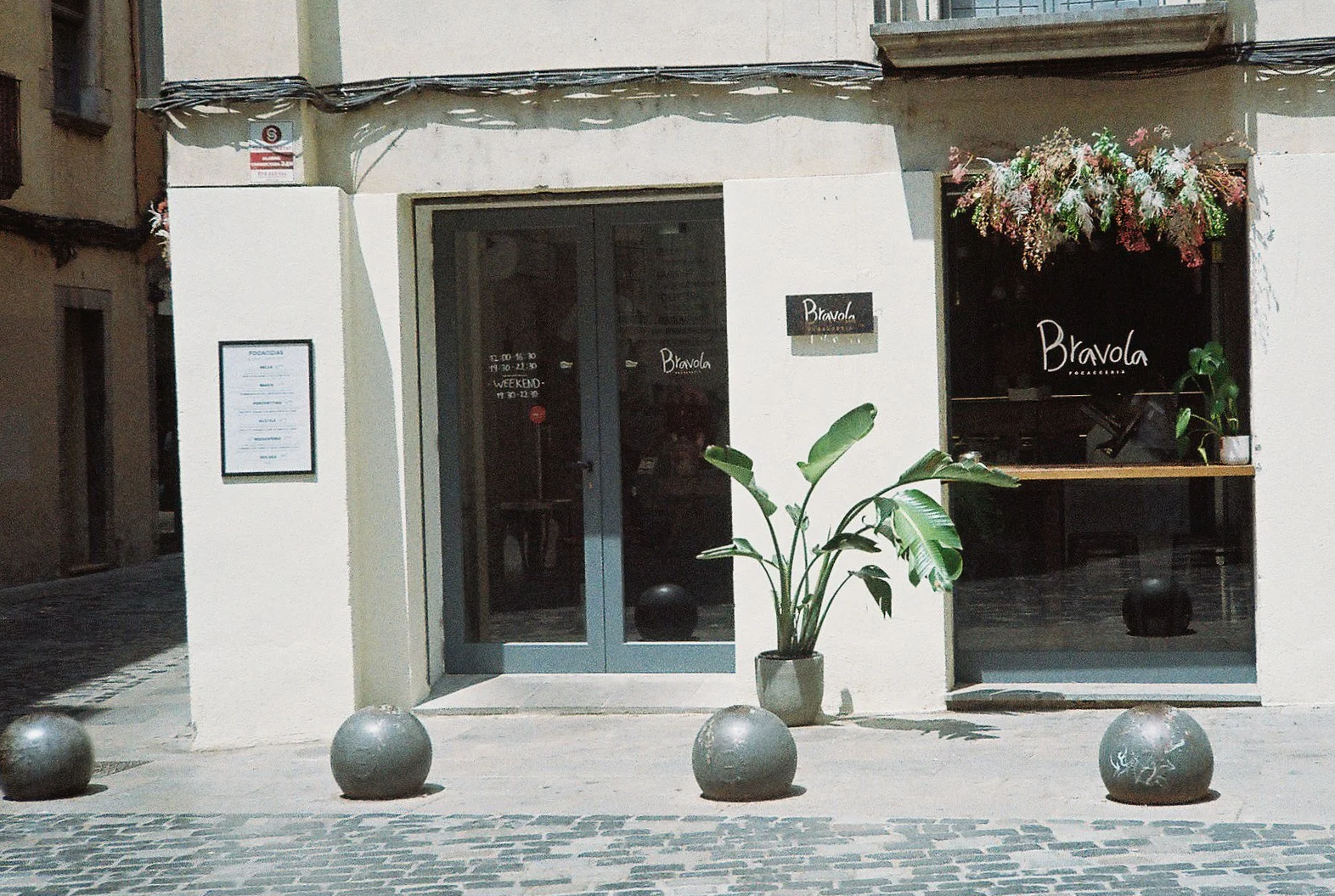 Fachada de una focacceria llamada Bravola con ventana decorada con flores y un cartel en la pared