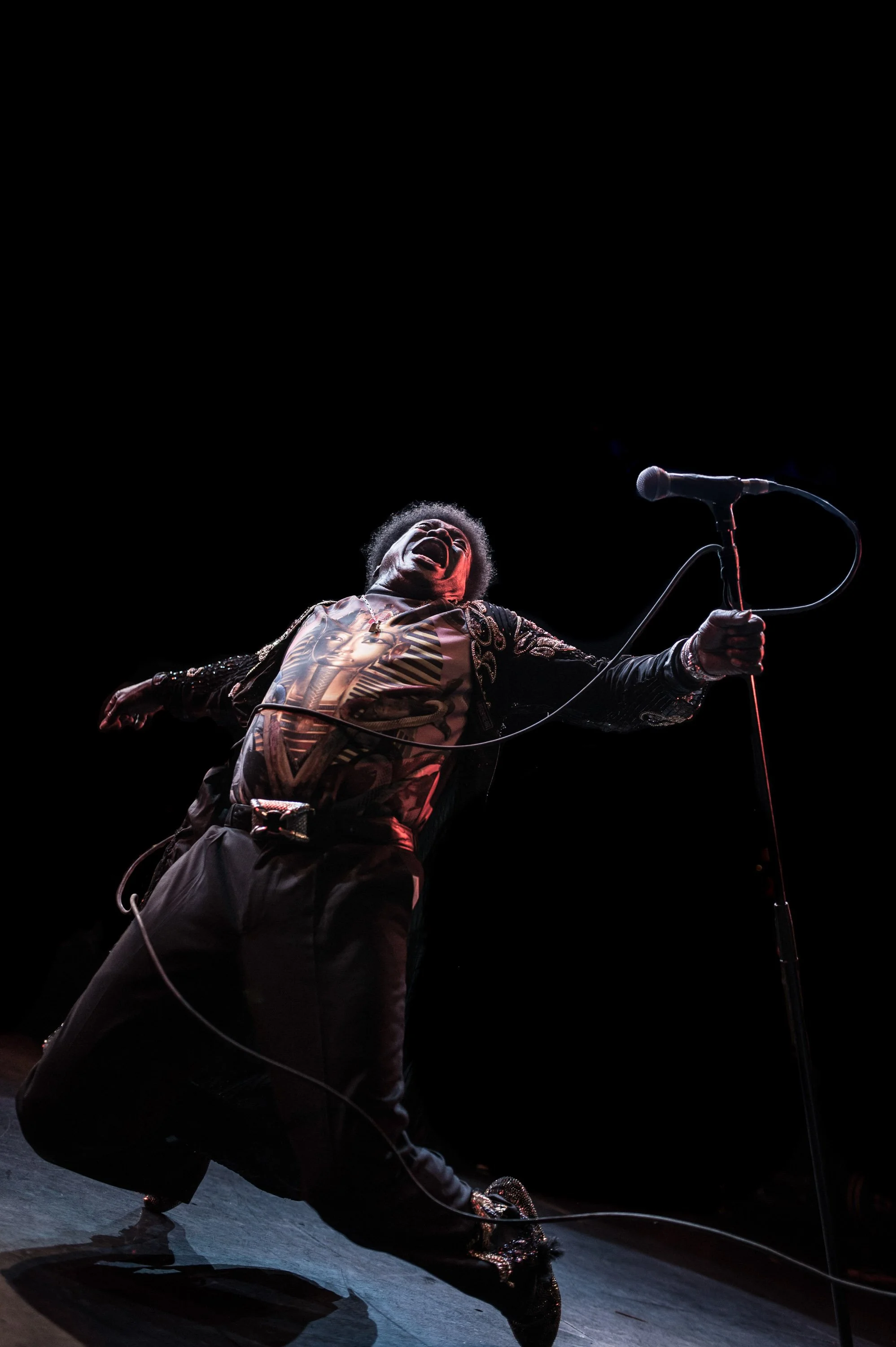 A singer leaning back on stage while holding a microphone stand.