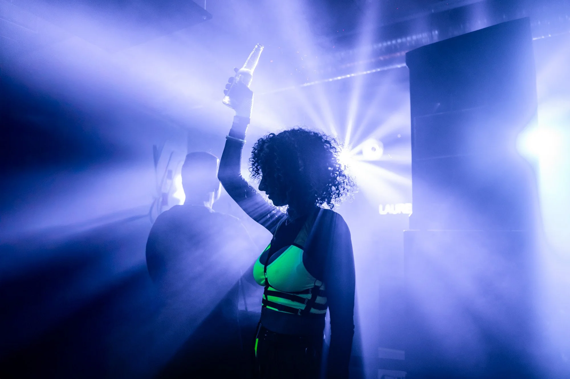 A woman raising one arm amid beams of blue and violet light.