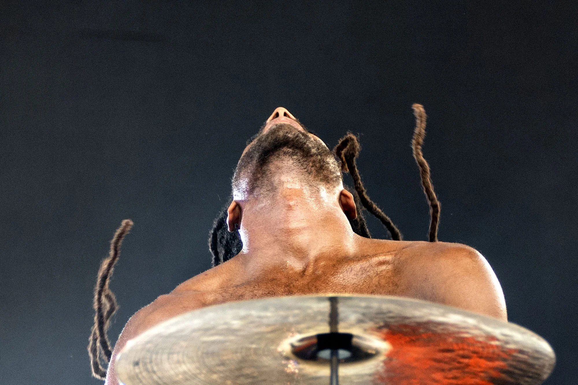 A drummer with his head tilted back behind a cymbal during a performance.