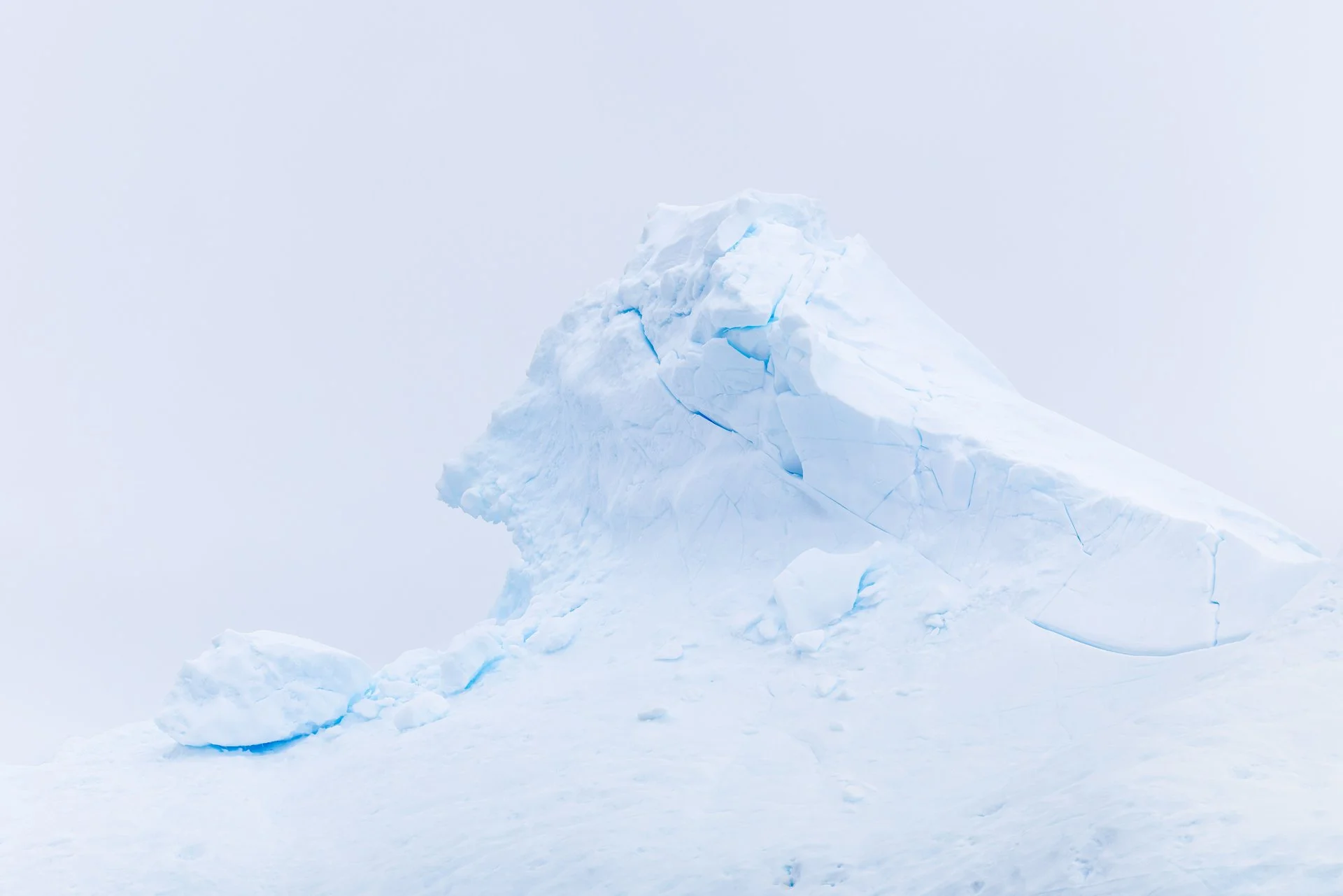 A large, jagged iceberg rising from the icy ocean with a clear, light blue sky in the background.