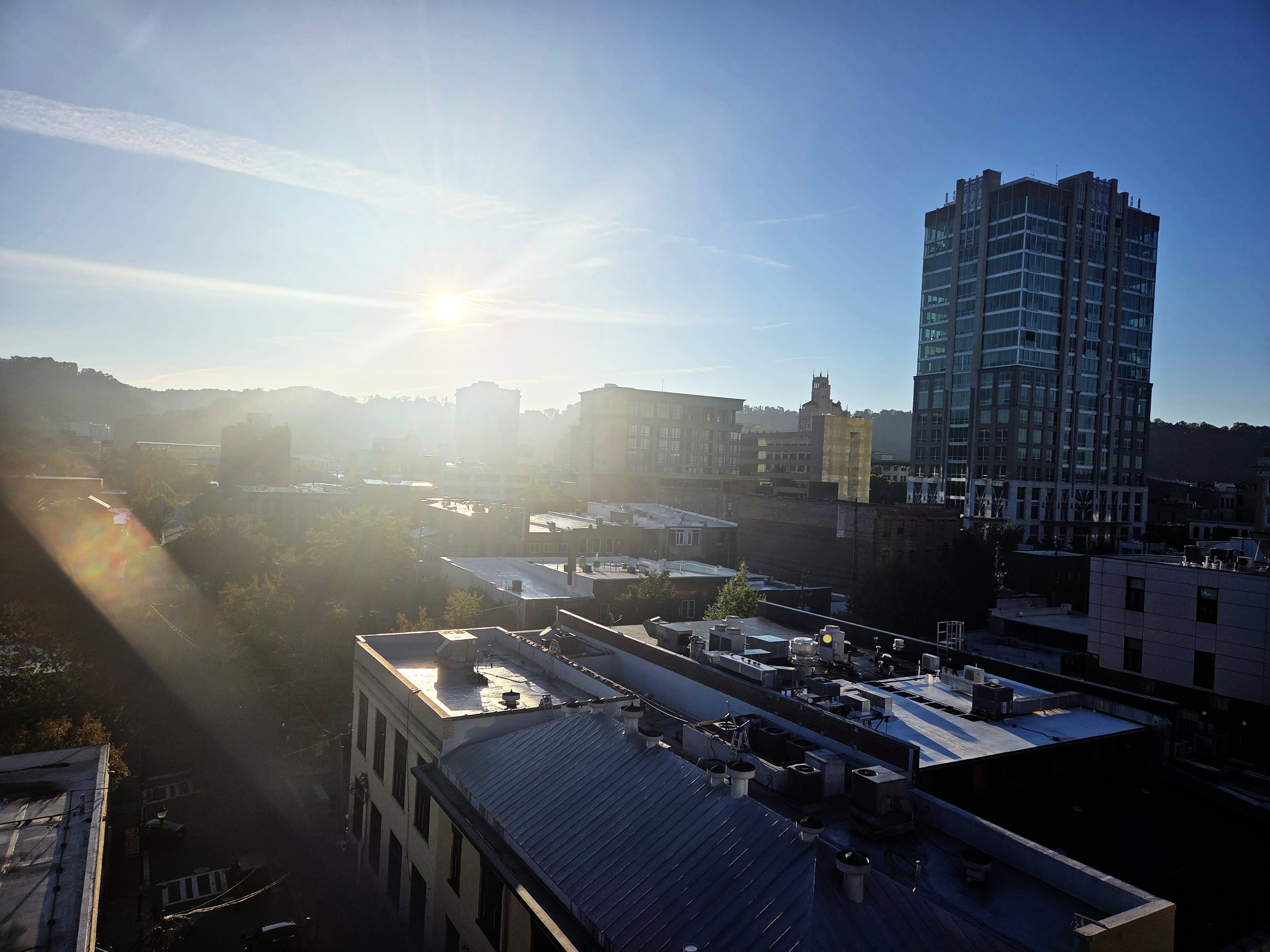 Sunlit cityscape with tall modern buildings and hills in the background.
