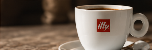 A white coffee cup with the illy logo, filled with coffee, on a saucer.