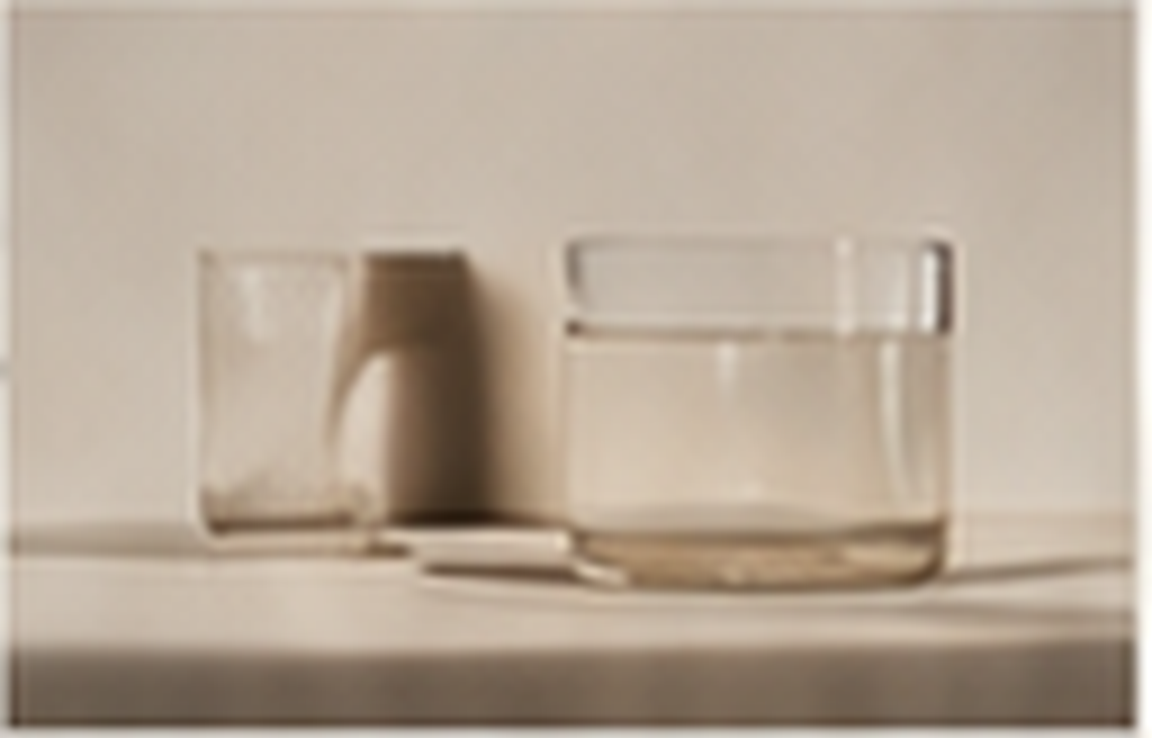 A desk holding an empty glass, a small pitcher, and a rectangular container- beauty.