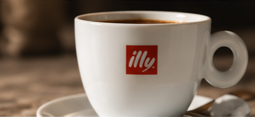 A white coffee cup with the illy logo, filled with dark coffee, on a matching saucer.