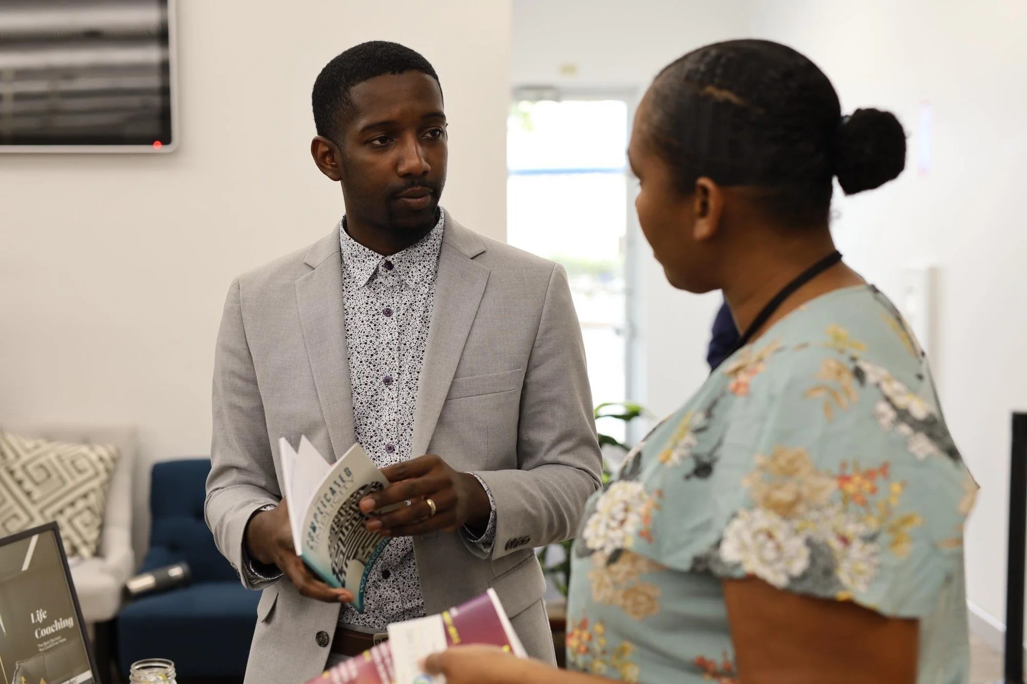 WJ Daggins in a grey blazer talking with a woman at a coaching event, his book open in his hand