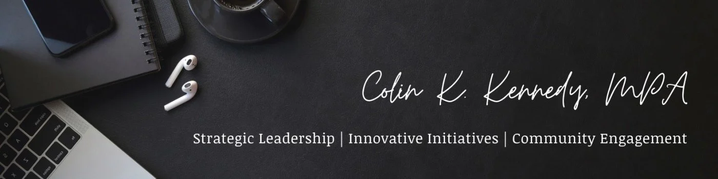 Business card with the name Colin K. Kennedy, MPA, and keywords: Strategic Leadership, Innovative Initiatives, Community Engagement on a black surface with AirPods, a smartphone, a notebook, and a laptop nearby.