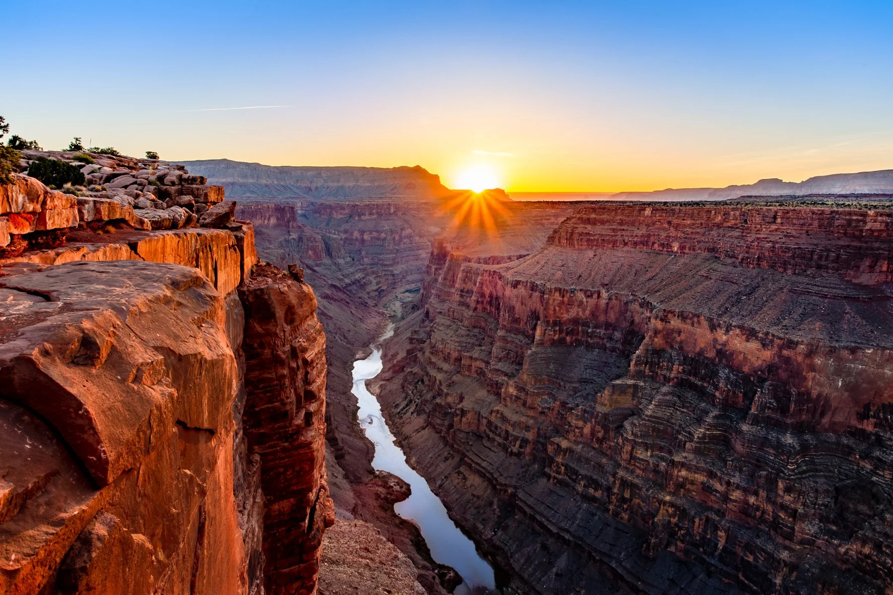 Sunset over the Grand Canyon showing layered red rock formations and the Colorado River at the bottom.
