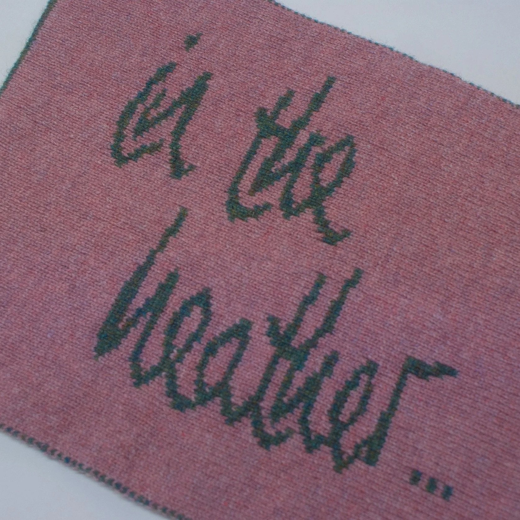 Close-up of a pink textured fabric with knitted letters reading 'in the heather'.