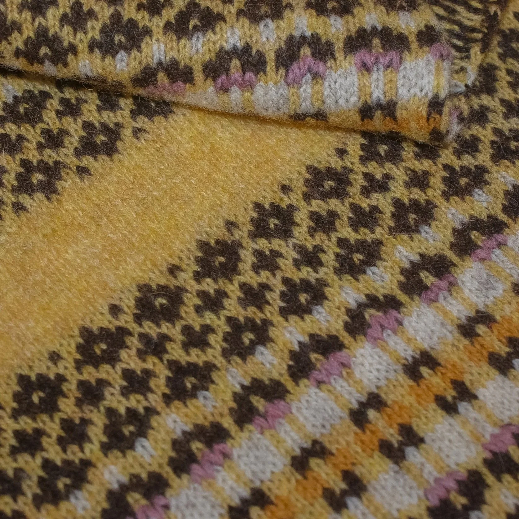 Close-up view of a knitted Fair Isle fabric with a pattern that includes black, yellow, white, pink, and orange colours.