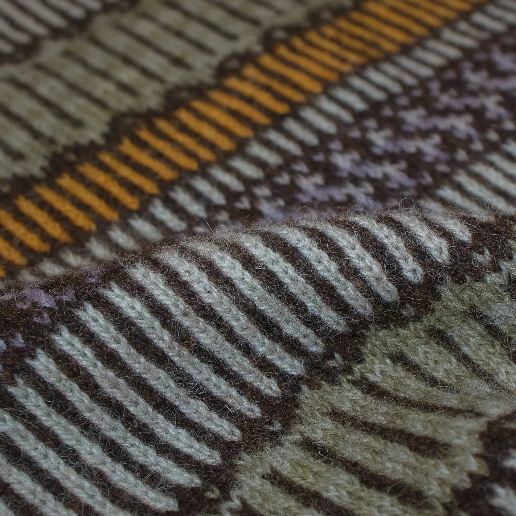 Close-up of a knitted Fair Isle fabric with alternating dark brown, beige, and orange threads, showing the texture and pattern of the textile.