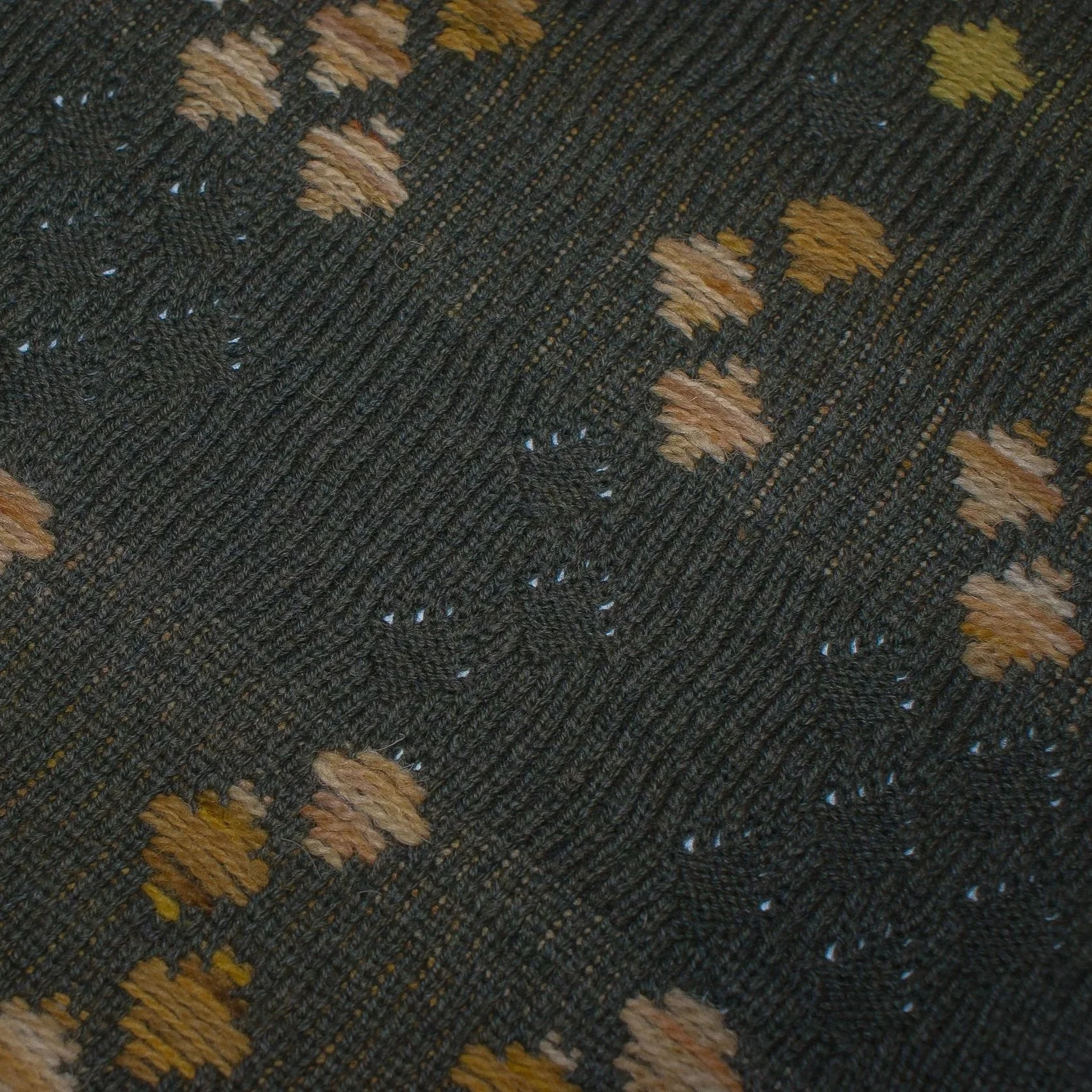 Close-up of a patterned knitted fabric with dark background and tan and yellow accents.