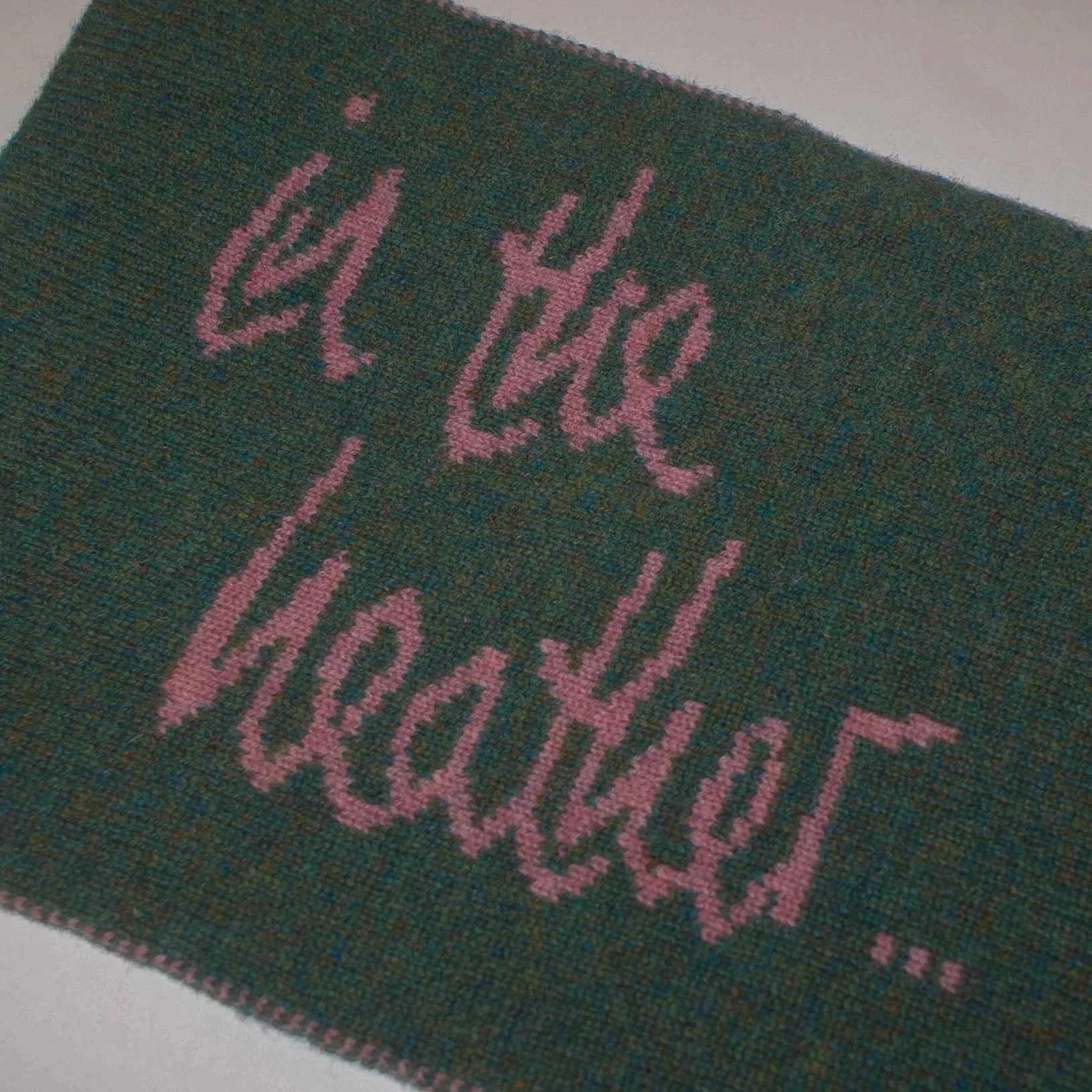 Close-up of a black fabric with pink embroidered letters reading 'in the heather'.