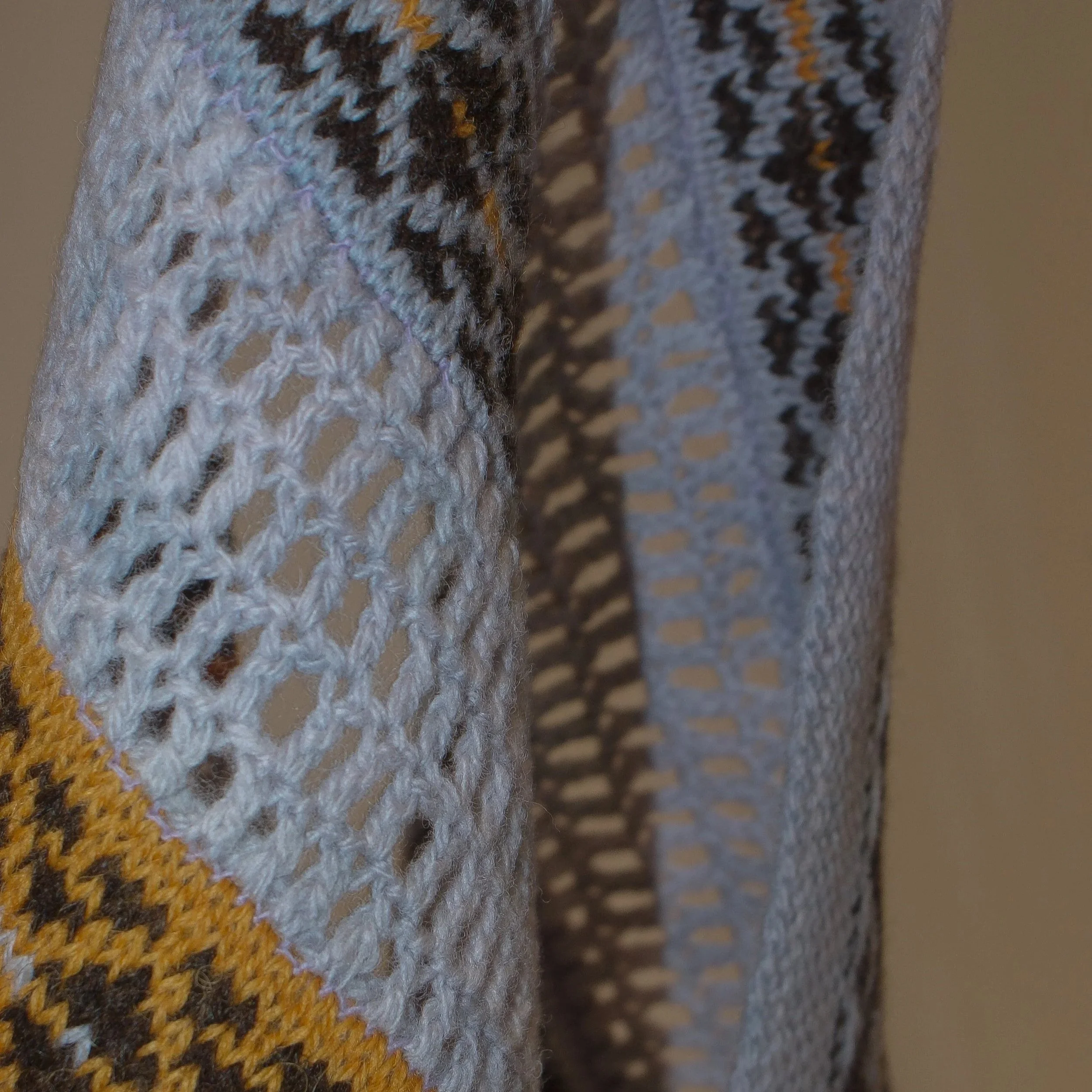 Close-up of a knitted and crocheted fabric with brown, gray, black, and yellow threads.