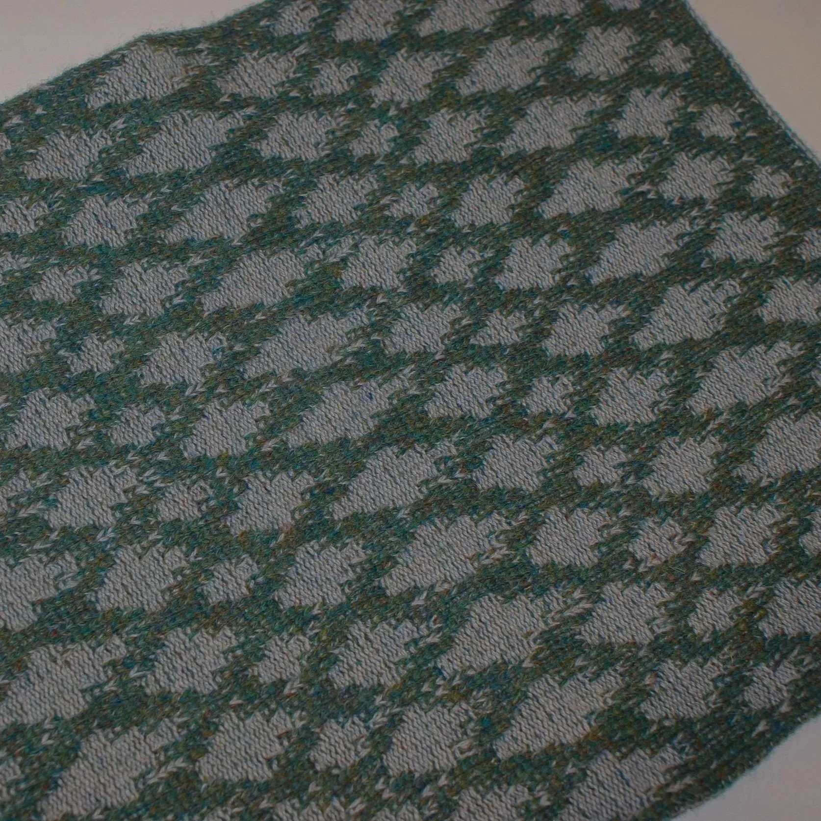 A close-up image of a brownish-green knitted fabric with a diamond pattern.