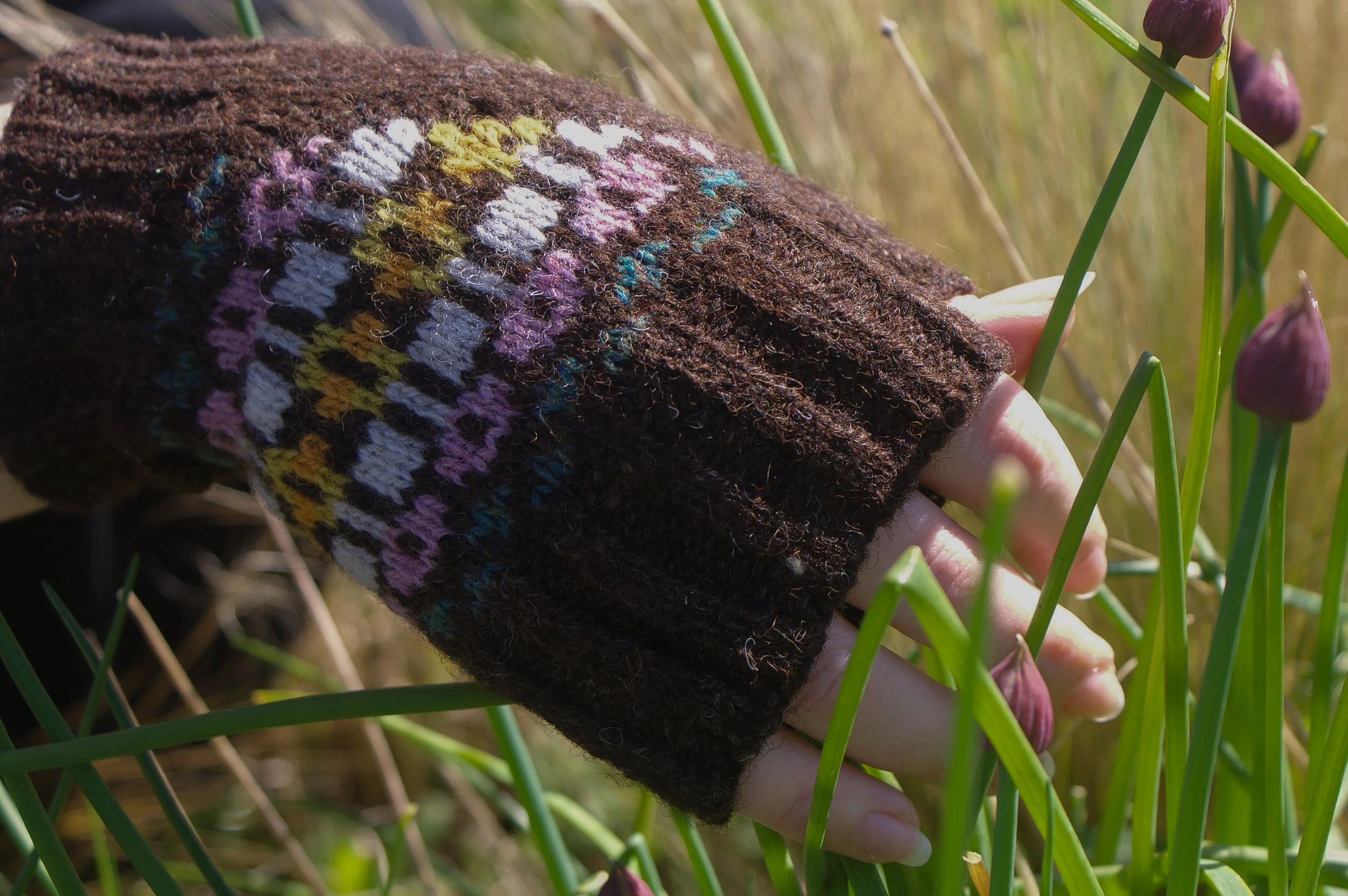 A hand with a brown knitted glove with colorful patterns.