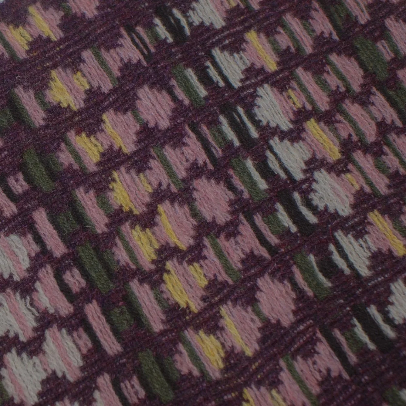 Close-up of a knitted textile with a diamond pattern in shades of pink, purple, yellow, white, and green.